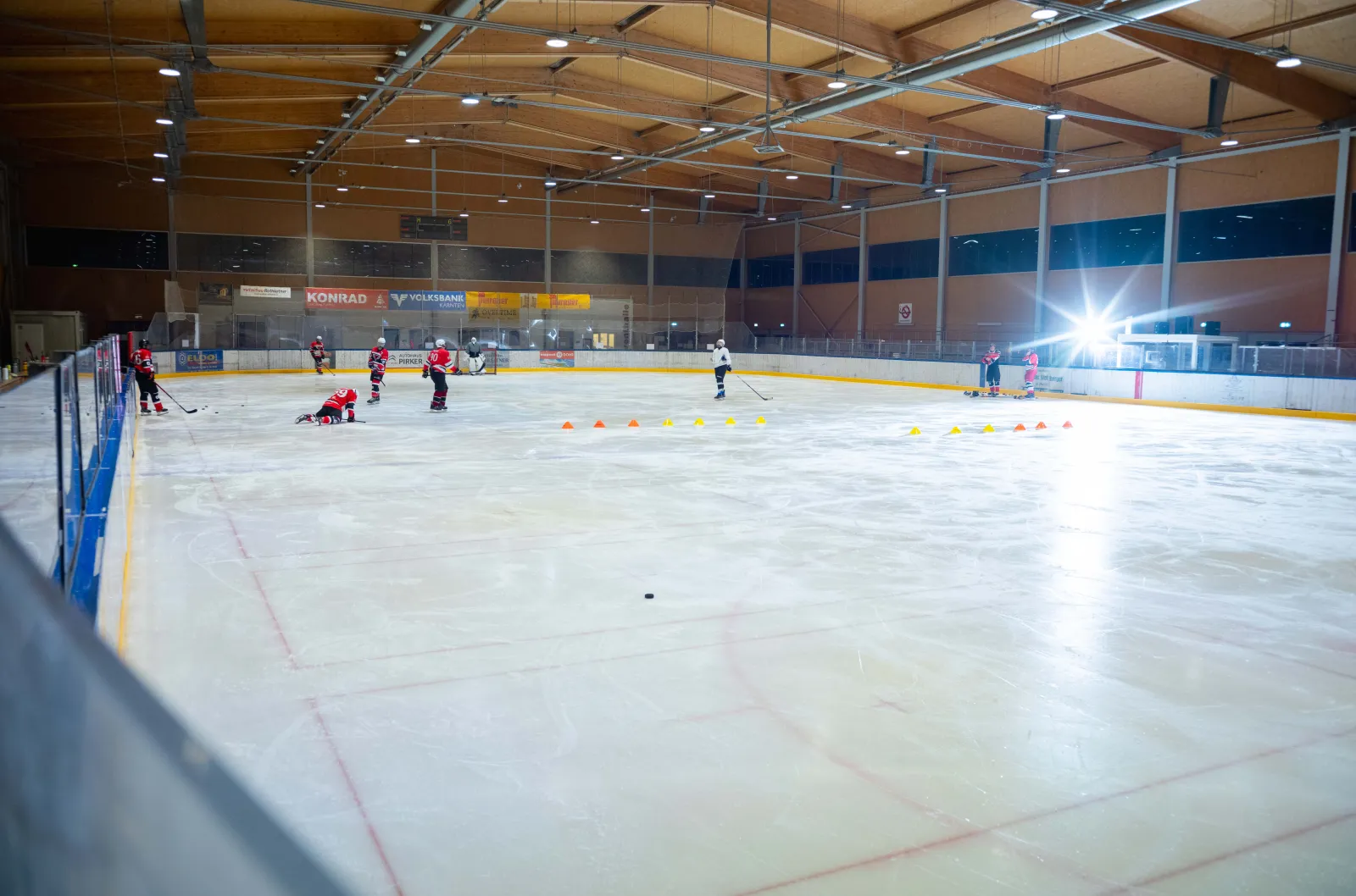 Die Eisfläche der Eventhalle Wolfsberg unter ihrem Holzdach, in der Ferne ein paar kleine Spieler – Eishalle Wolfsberg (Eventhalle Kleinedling)