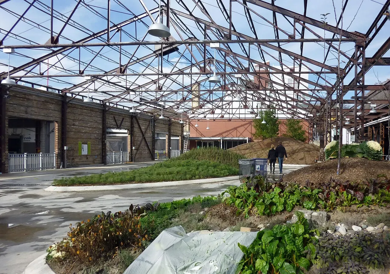 The roofed Koerner Gardens structure at Evergreen Brick Works in its ice-free configuration: exposed steel roof trusses over brick factory walls, with the garden paths that become the winter rink. — Evergreen Brick Works Skating Rink