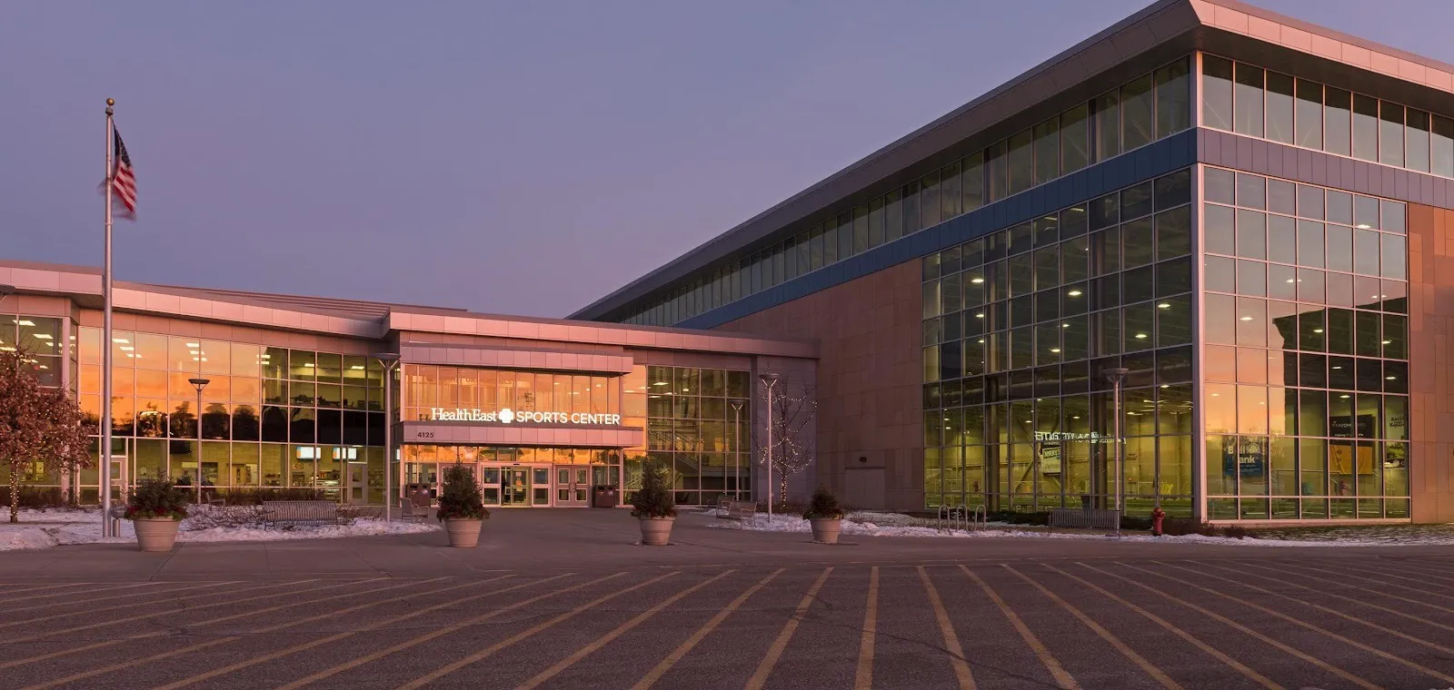 The sports center entrance at 4125 Radio Drive at dusk, still signed with its earlier HealthEast name, beside the tall glass fieldhouse — M Health Fairview Sports Center