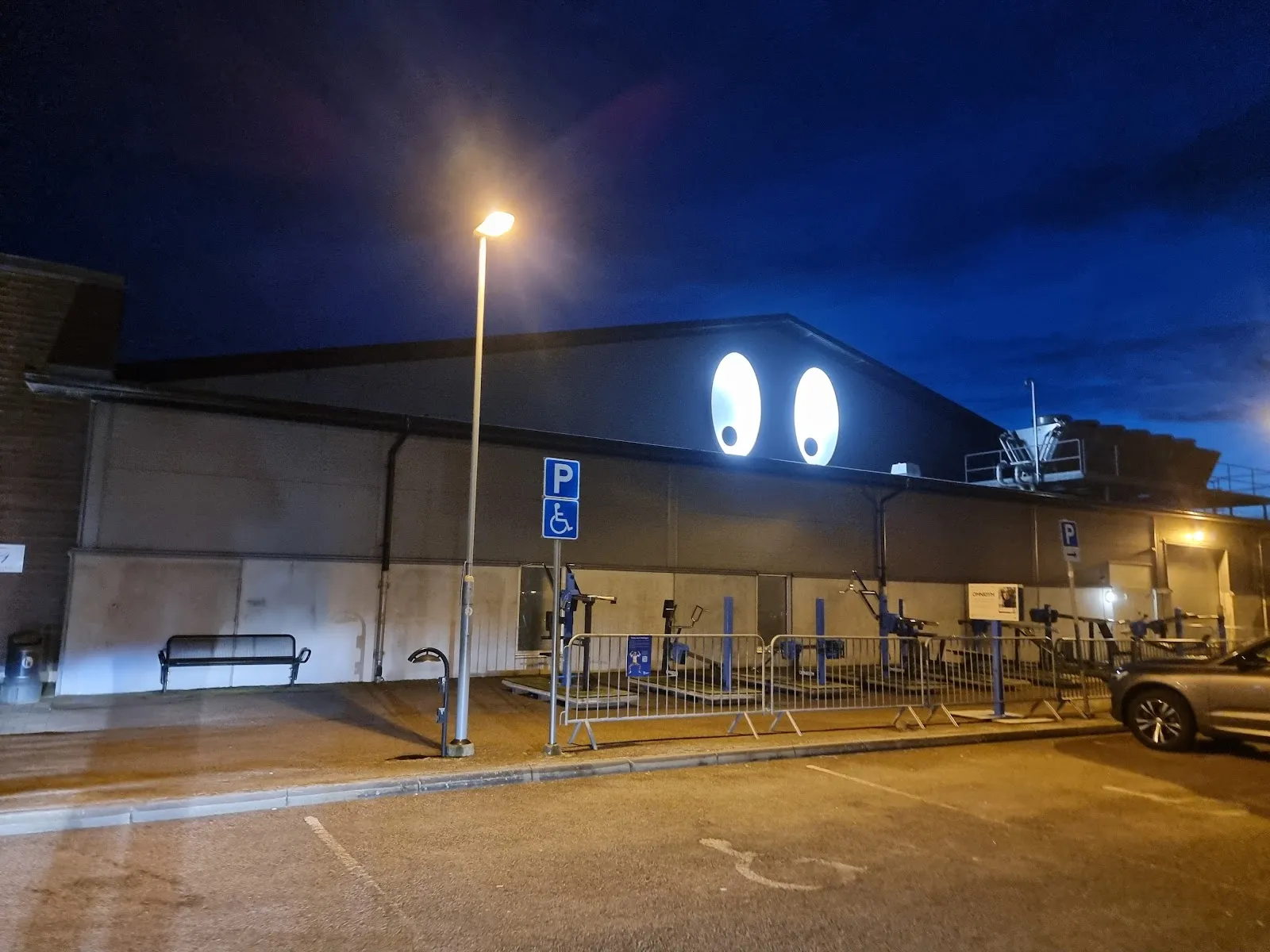 The side of Falkenbergs ishall at night, with the two lit eyes on the gable above the car park — Falkenbergs ishall