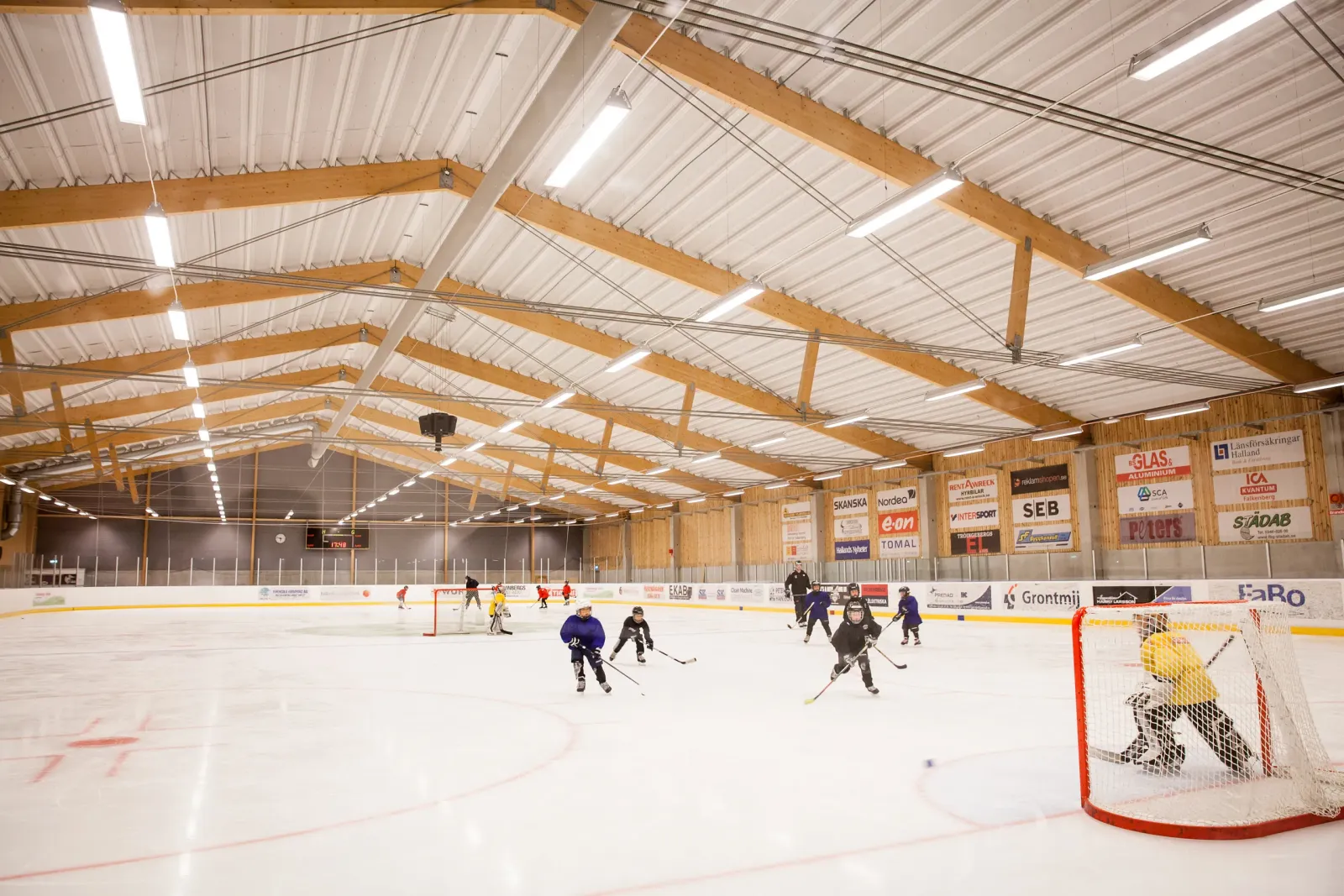 The ice at Falkenbergs ishall under its timber-beam roof, with youth hockey players practising on the sheet — Falkenbergs ishall