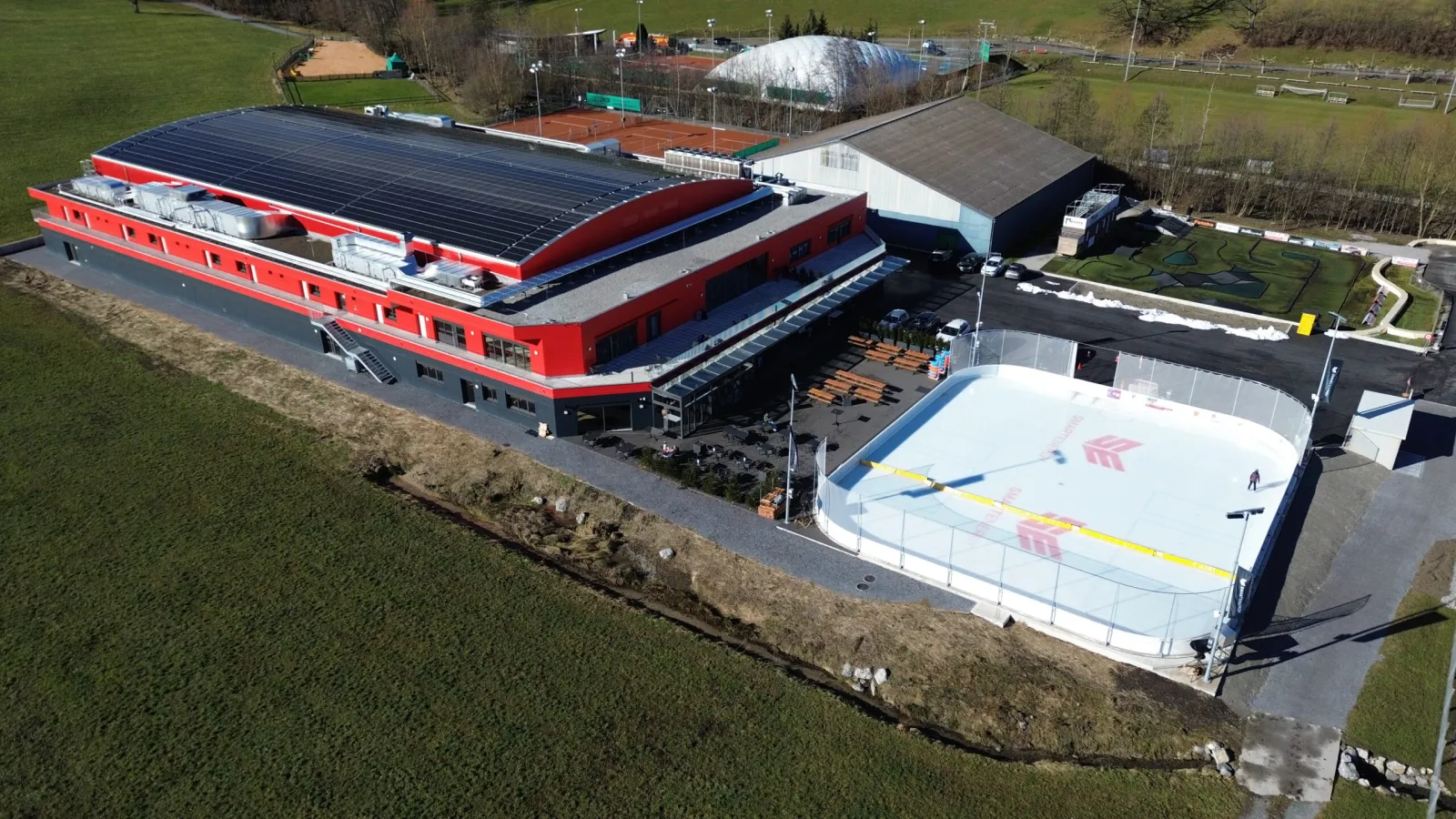 Luftaufnahme des FarFar Ice Camps in Wollerau, die Eishalle mit roter Front, davor das Aussen-Eisfeld Ausseneisfeld – FarFar Ice Camp Wollerau (Ausseneisfeld)