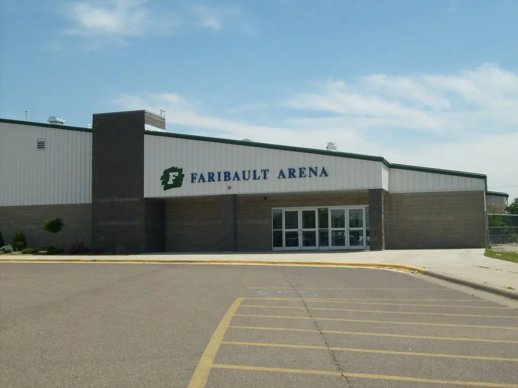 The front of the arena with FARIBAULT ARENA lettering over the glass entrance and an empty parking lot. — Faribault Ice Arena