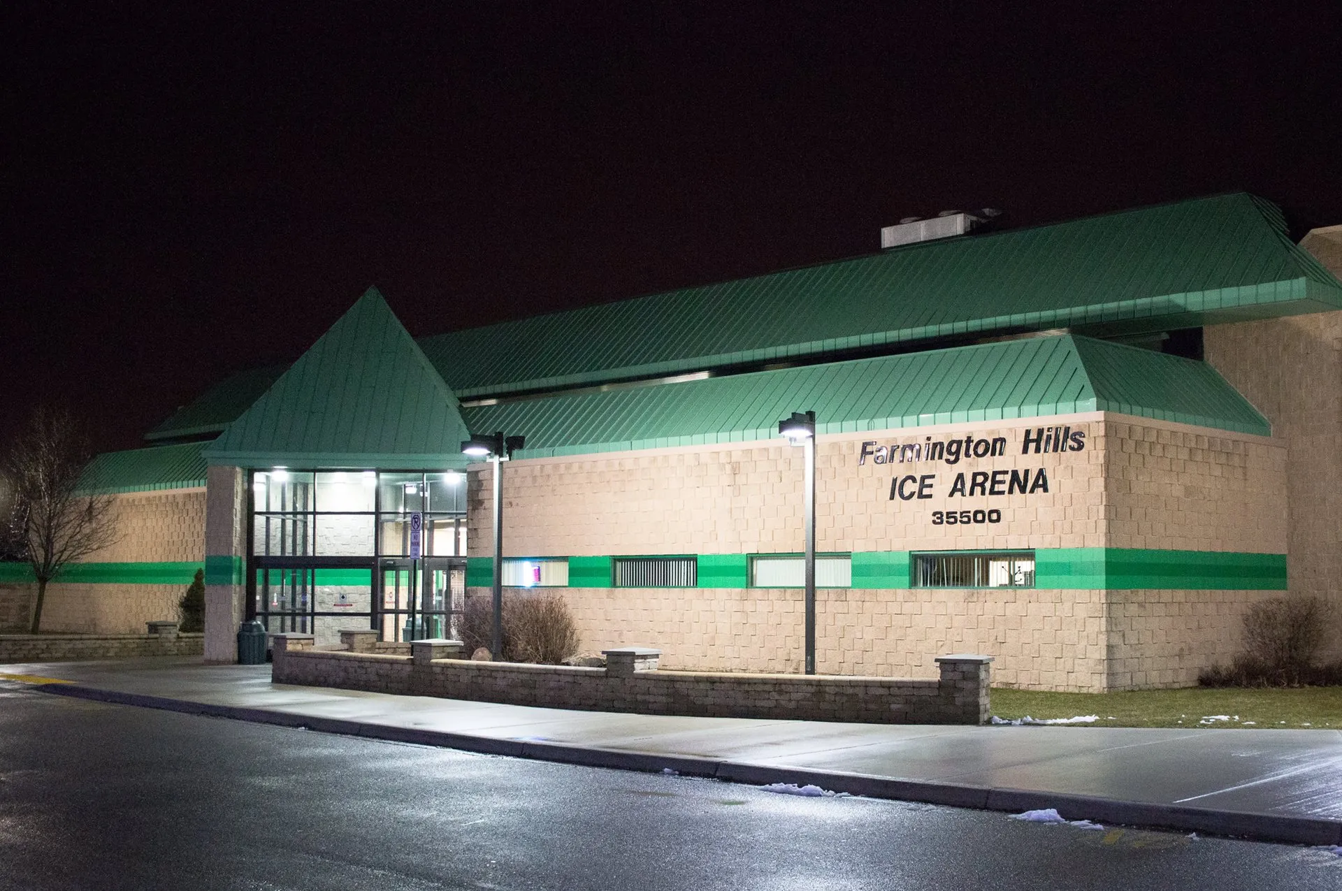La entrada de vidrio iluminada bajo techos verdes de noche — Farmington Hills Ice Arena