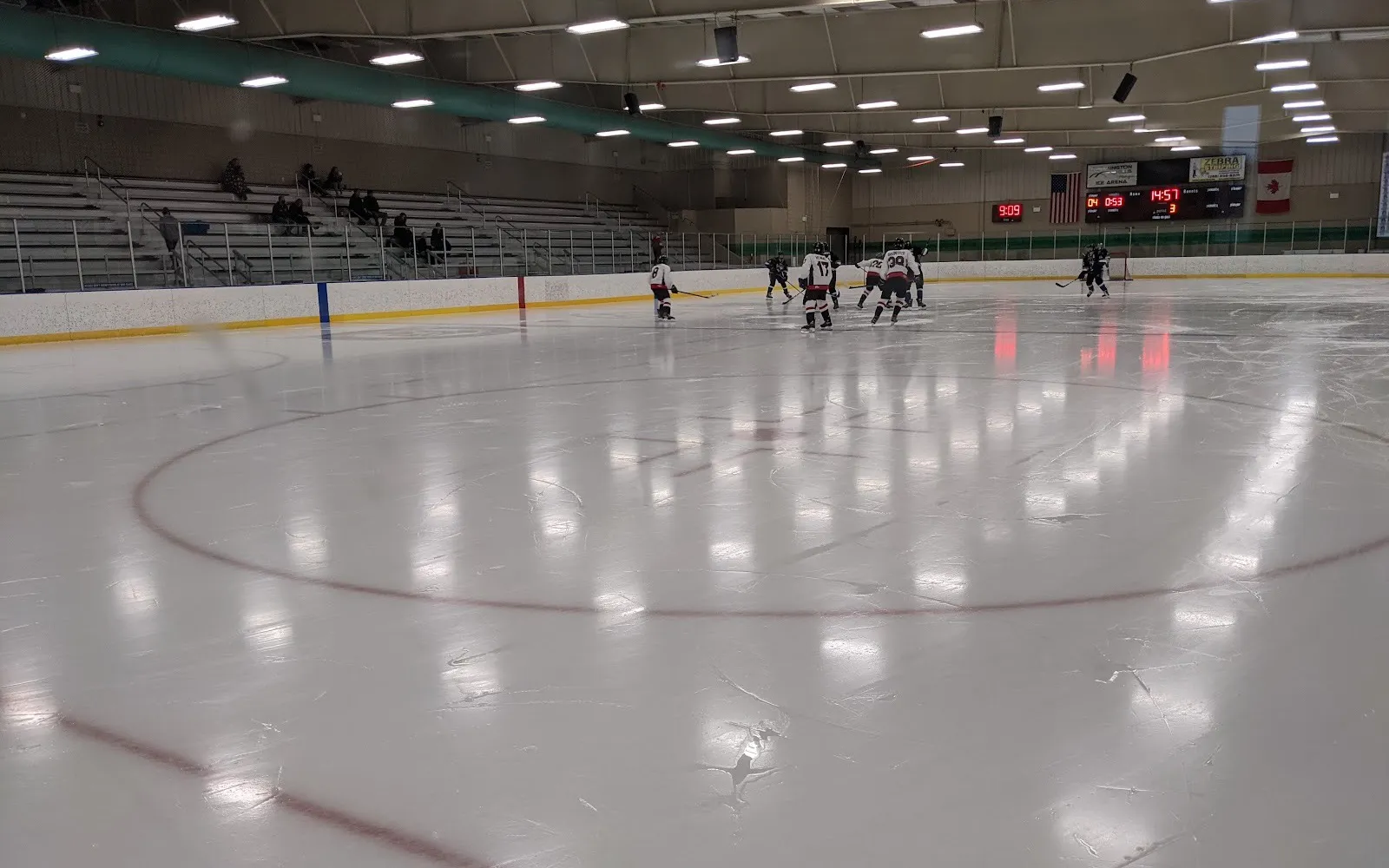 Una pista de Farmington Hills desde el vidrio en el centro del hielo, con las gradas, el marcador de la arena y un partido juvenil en el extremo opuesto — Farmington Hills Ice Arena