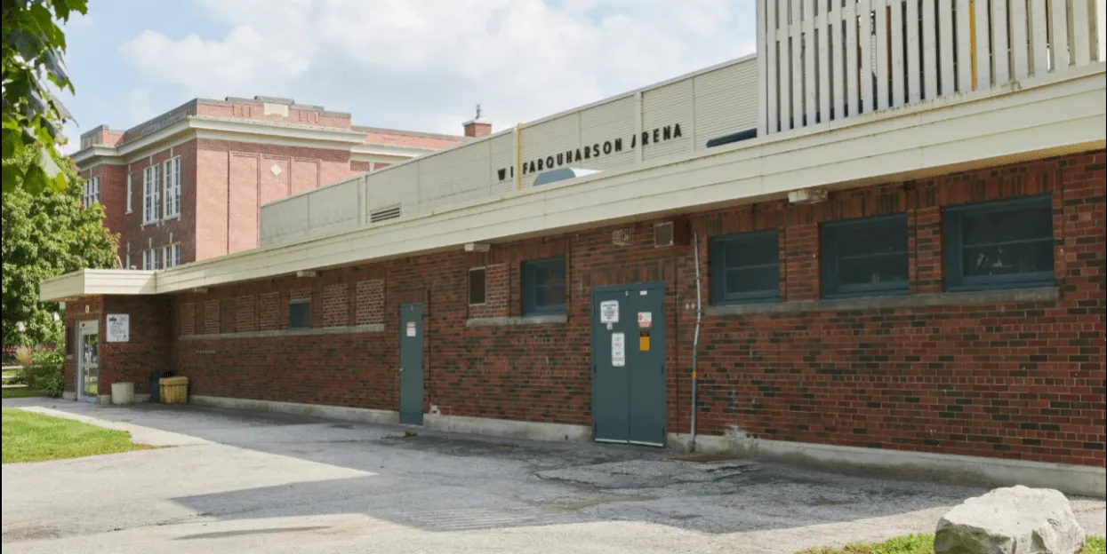 The brick side of the arena on Tecumseh Avenue East, with W.J. FARQUHARSON ARENA lettered along the upper wall. — Farquharson Arena