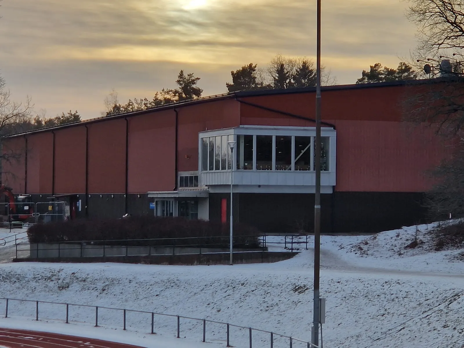Farsta ishall, the red-clad hall with its glazed entrance block, at dusk — Farsta ishall