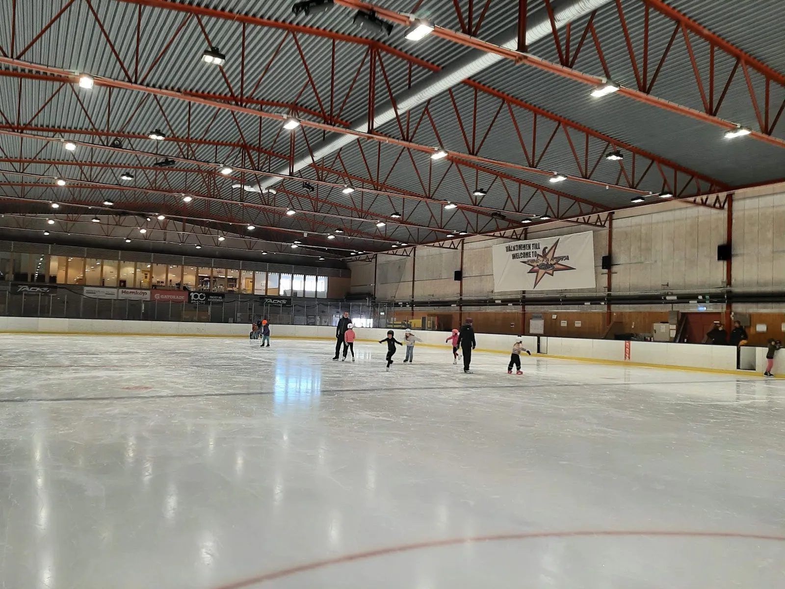 Ice of Farsta ishall under the red steel roof, with skaters at the far end — Farsta ishall