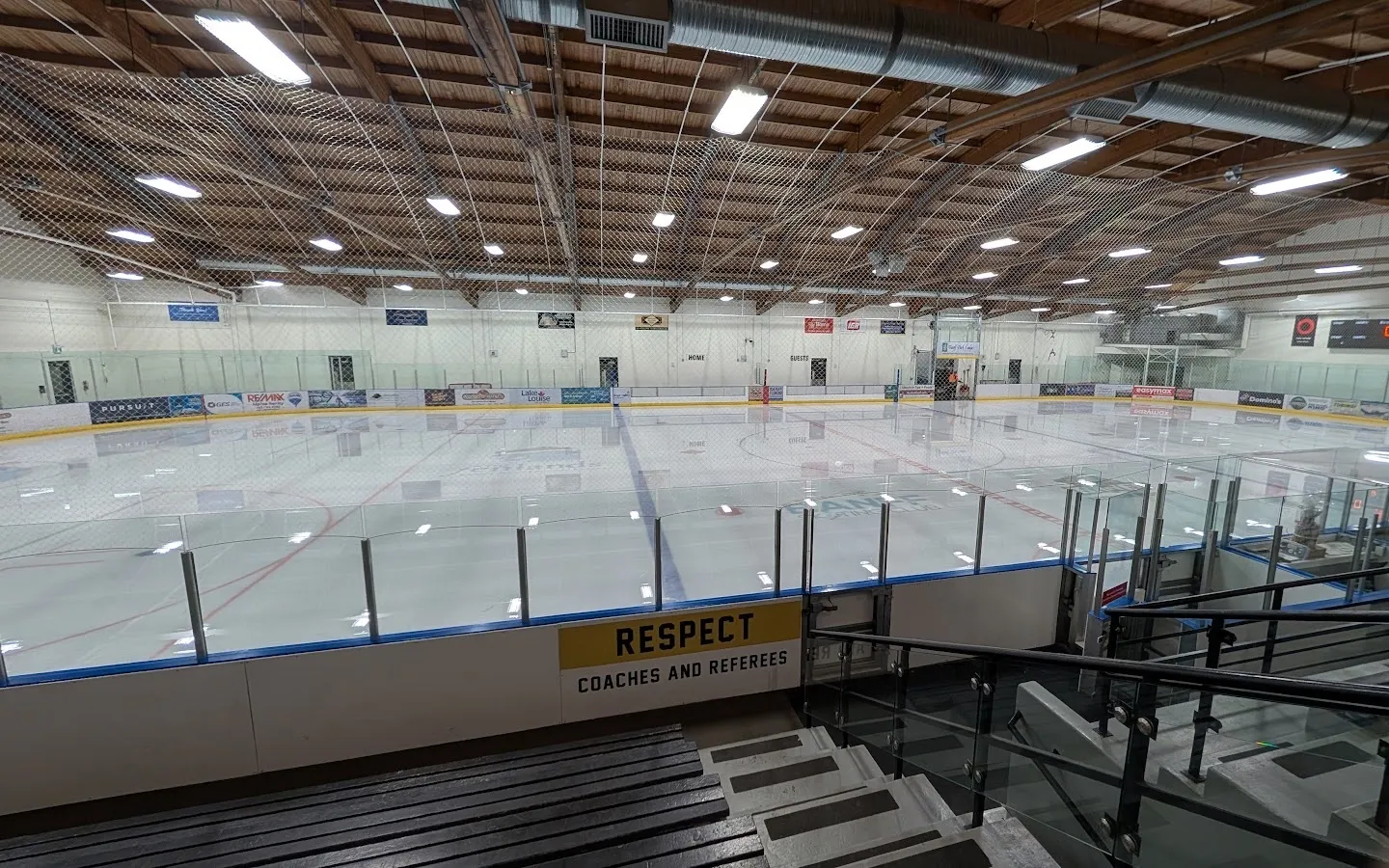 Una pista vacía bajo las vigas de madera curvas del techo del centro Fenlands, vista desde las gradas más allá de un letrero de Respect Coaches and Referees. — The Fenlands Banff Recreation Centre
