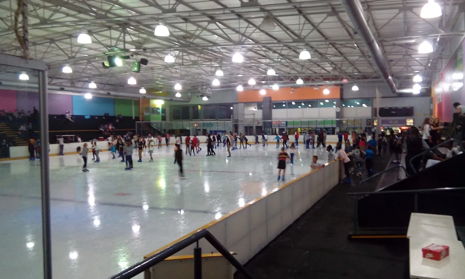 The ice sheet of the Festival Mall Ice Rink with skaters spread along the far side under the lit roof — Festival Mall Ice Rink