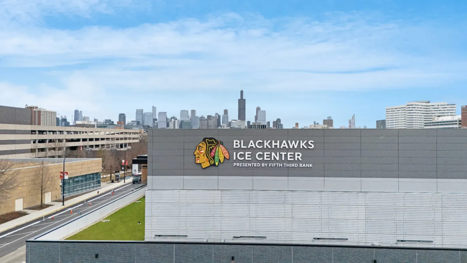 The grey upper wall of the arena carrying the Blackhawks head logo and "BLACKHAWKS ICE CENTER, PRESENTED BY FIFTH THIRD BANK" in white lettering, with the downtown Chicago skyline and Willis Tower behind it. — Fifth Third Arena (Blackhawks Ice Center)