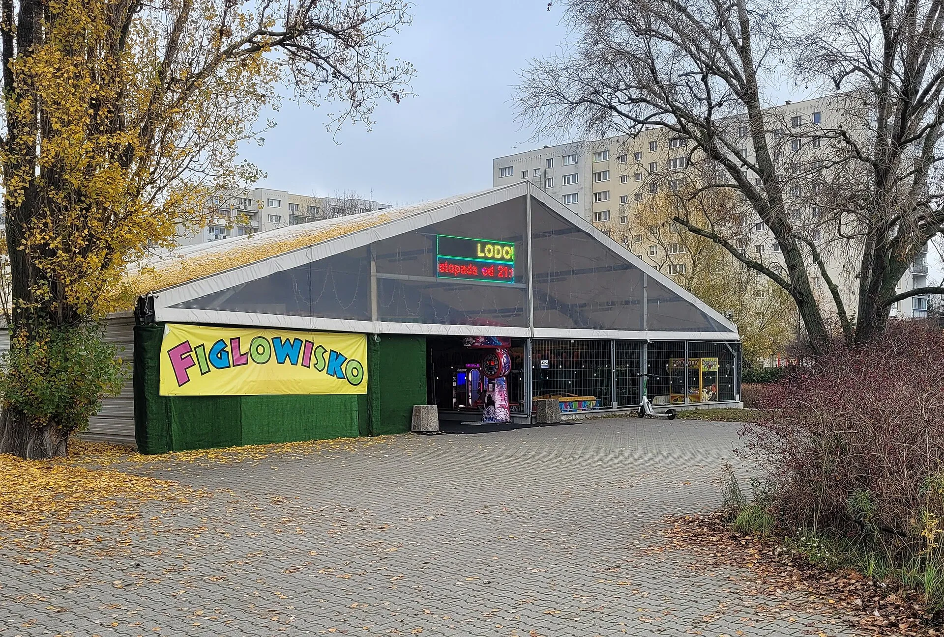 The glazed tent hall of the Figlowisko rink on Al. KEN in Warsaw Ursynów, with the Figlowisko banner at its entrance — Figlowisko Lodowisko 24h