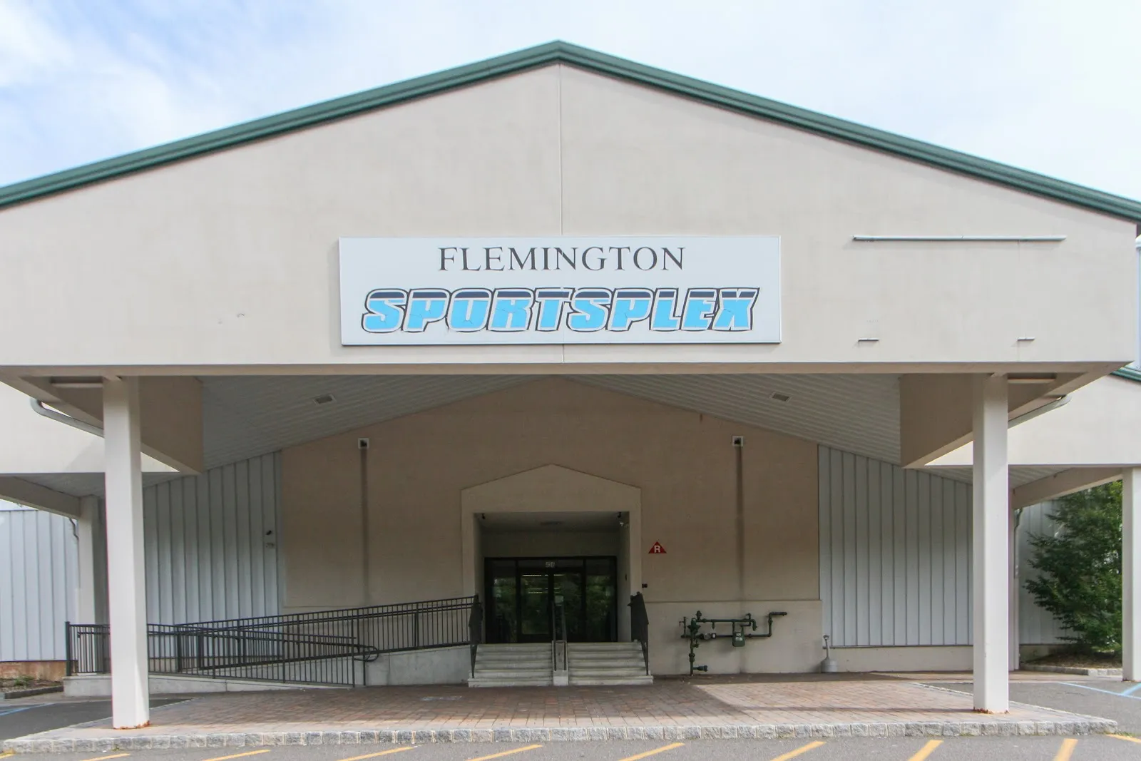 Entrada principal del edificio de Flemington Sportsplex bajo un frontón de techo verde, con un letrero de 'FLEMINGTON SPORTSPLEX' sobre el acceso techado. — Flemington Ice Arena