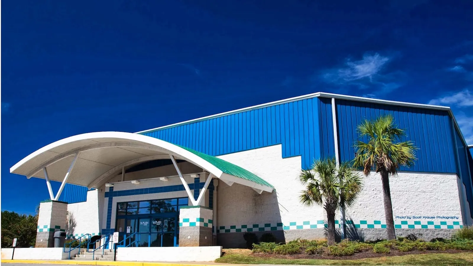El edificio azul de techo curvo de Flight Adventure Park Irmo, que alberga la pista de hielo, con palmeras en la entrada. — Flight Adventure Park Irmo (ice rink)