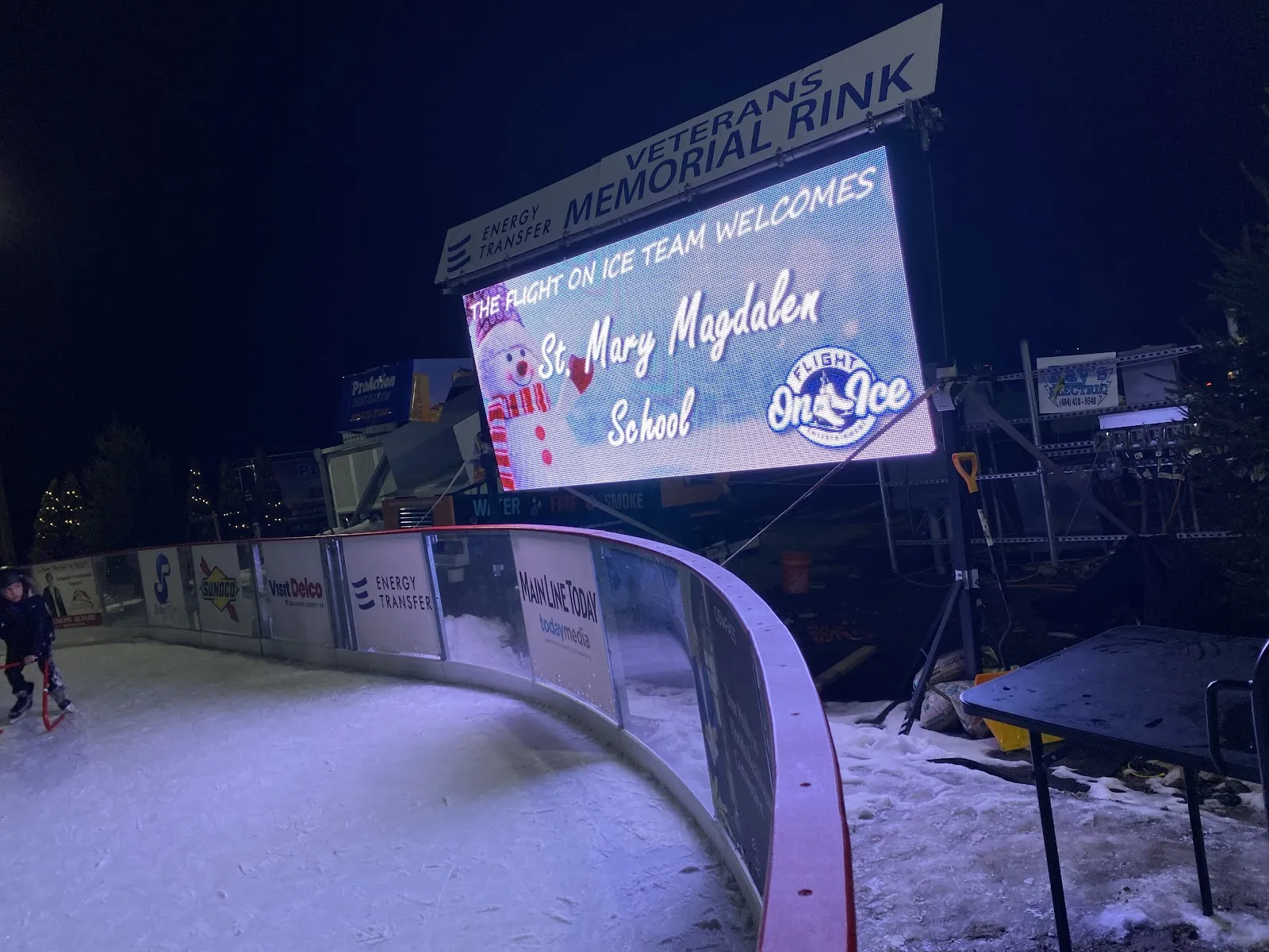 The Newtown Square rink after dark with a lit video screen above the boards and the ice mostly clear. — Flight on Ice Newtown Square
