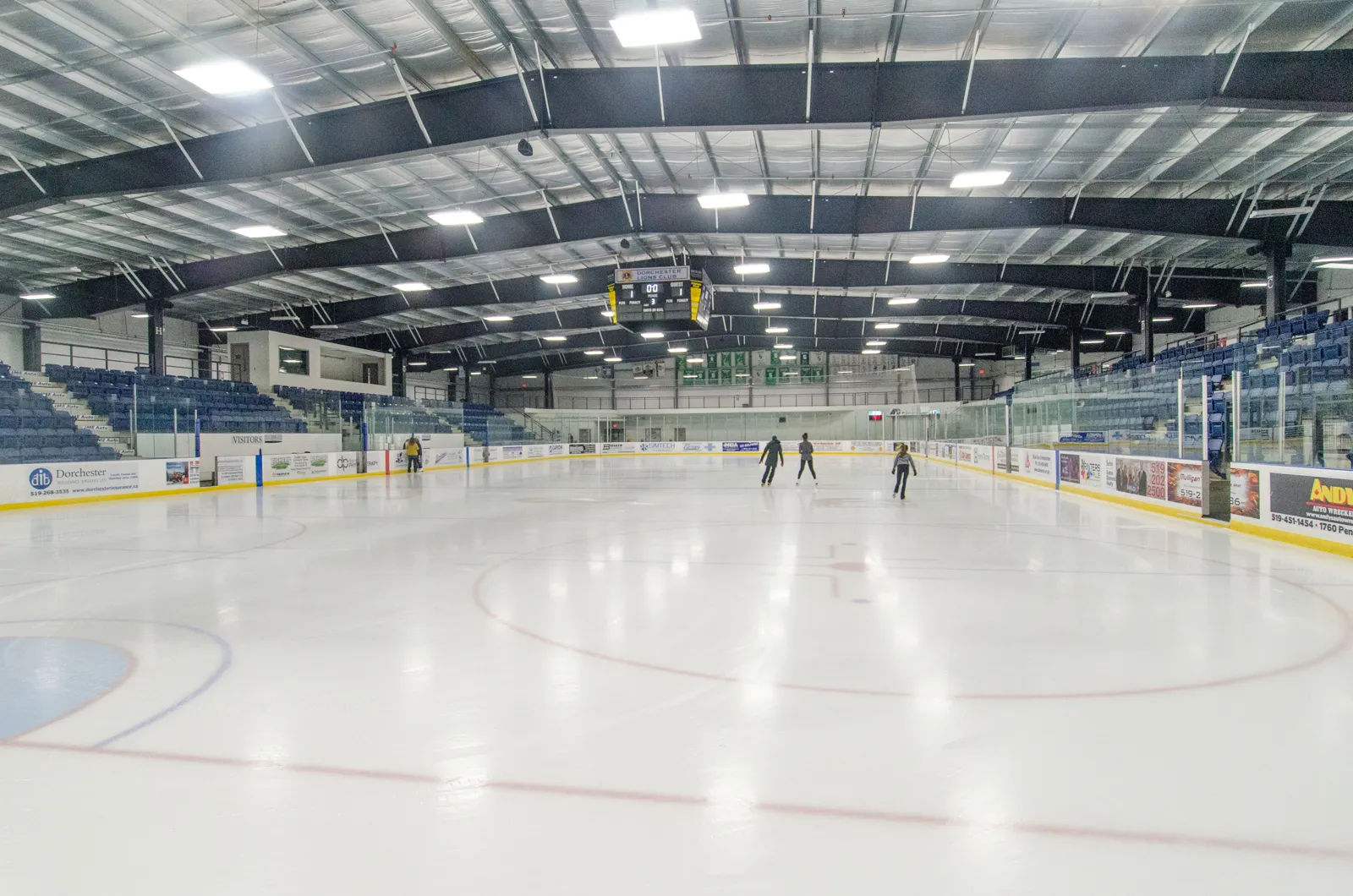 Una pista completa bajo el techo de acero, con asientos azules a ambos lados y algunos patinadores en el extremo opuesto. — FlightExec Centre (Dorchester)