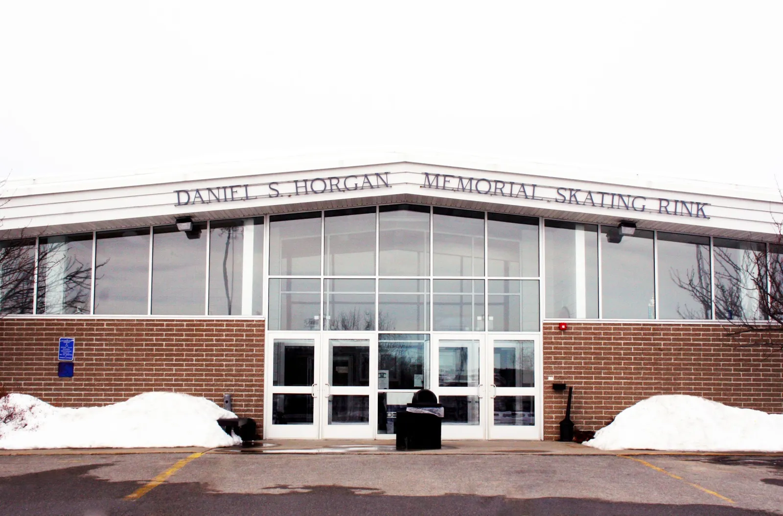 The brick-and-glass front of the building in winter, with "Daniel S. Horgan Memorial Skating Rink" lettered across the top and snow piled beside the entrance. — Horgan Arena