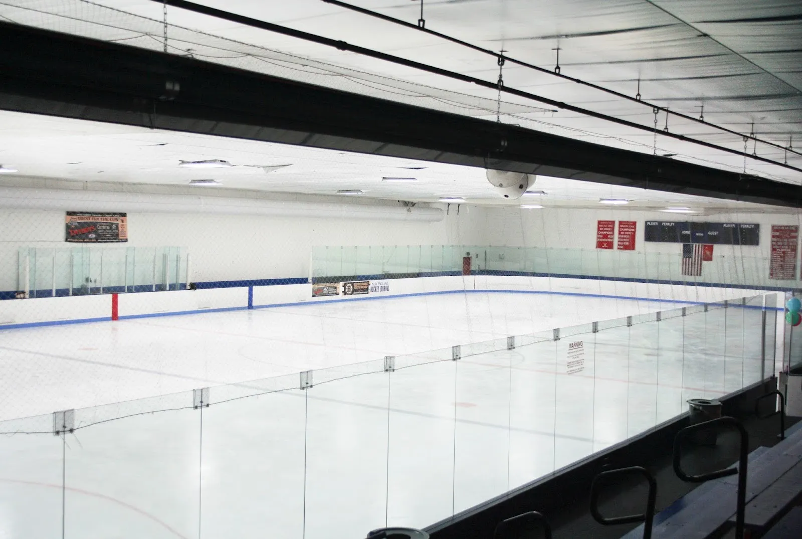 The empty ice at the Burlington Ice Palace, seen from the bleachers through the glass toward the scoreboard — Burlington Ice Palace