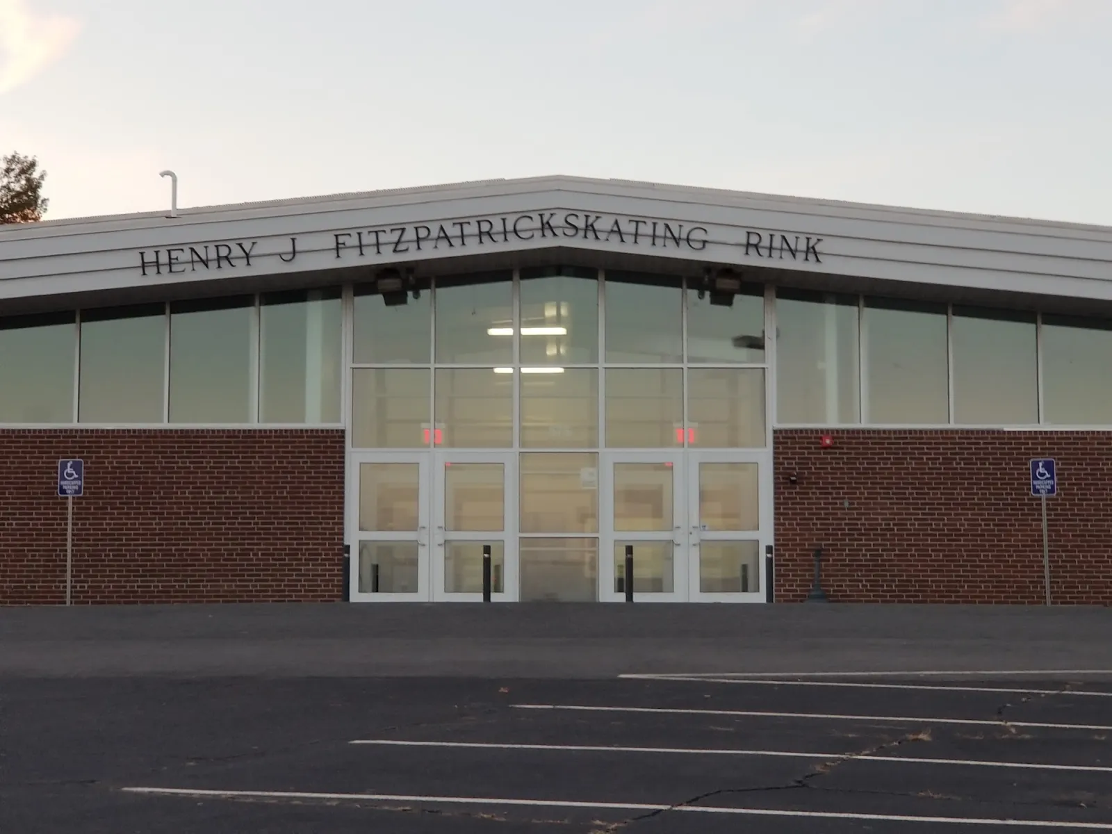 Front entrance of the Henry J. Fitzpatrick Skating Rink, a brick building with "HENRY J FITZPATRICK SKATING RINK" lettered above tall glass entrance doors and an empty parking lot in front. — Fitzpatrick Arena