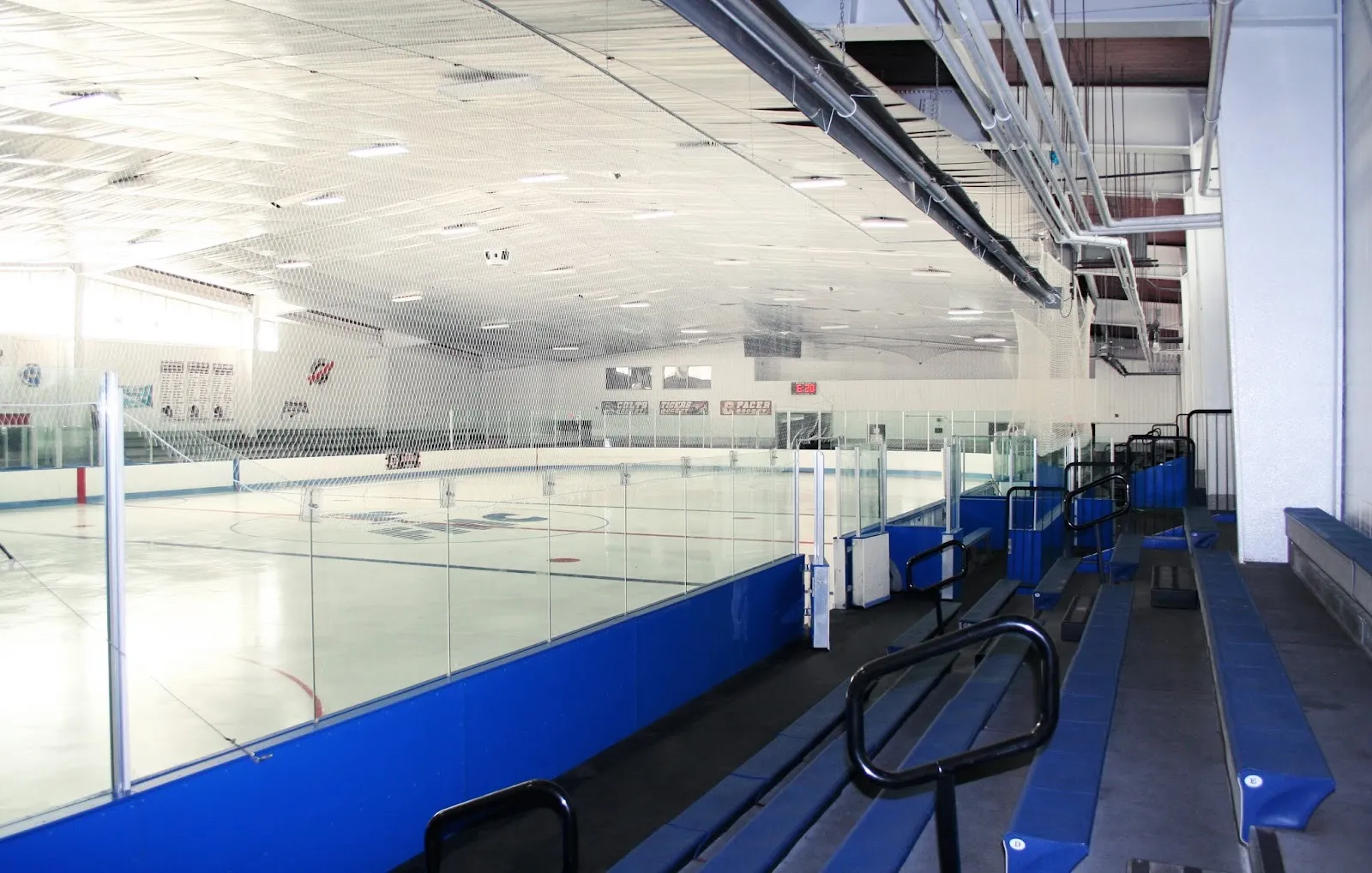 The empty Fitzpatrick Arena rink from the blue bleachers, the FMC logo at centre ice under a white netted roof — Fitzpatrick Arena