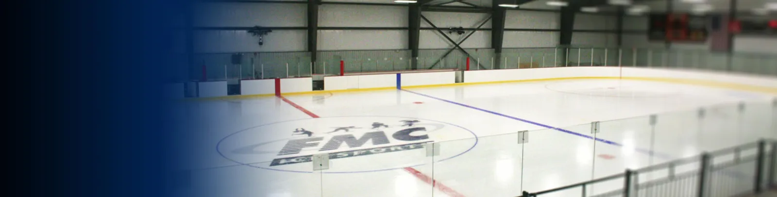 Wide view down the length of the ice sheet with red and blue hockey lines, glass boards, an FMC logo decal at center ice, and steel roof trusses overhead — Blackstone Valley IcePlex