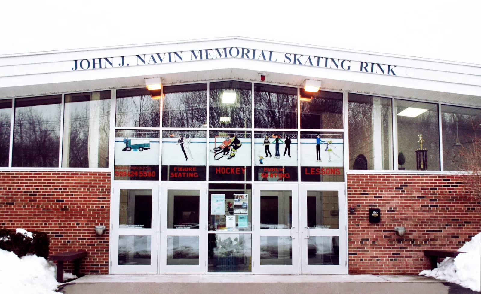 Front entrance of the John J. Navin Memorial Skating Rink, a brick building with the rink name lettered above a row of glass doors labelled Figure Skating, Hockey, Public Skating and Lessons. — Navin Arena