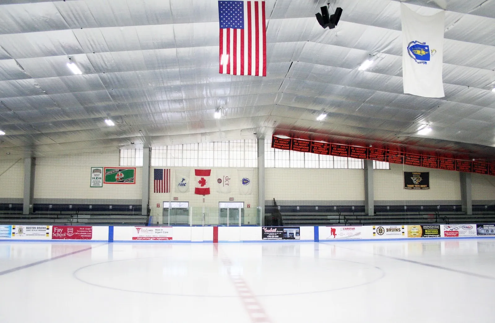 Empty ice at Navin Arena from centre ice, flags and championship banners hanging beneath a silver insulated roof — Navin Arena