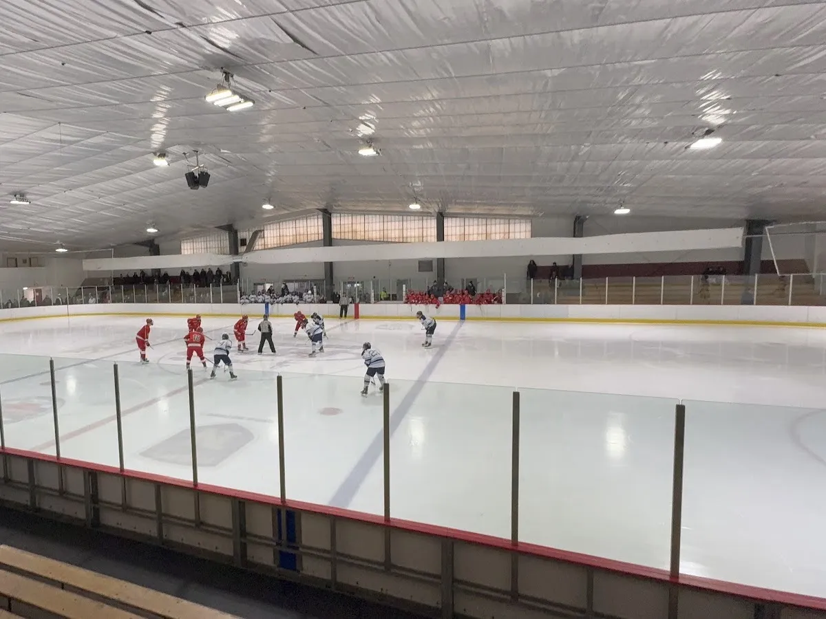 Amplia vista interior de toda la pista desde las gradas, con las vallas, el cristal, la estructura del techo y un partido de hockey en curso. — Henry Graf Jr. Memorial Rink
