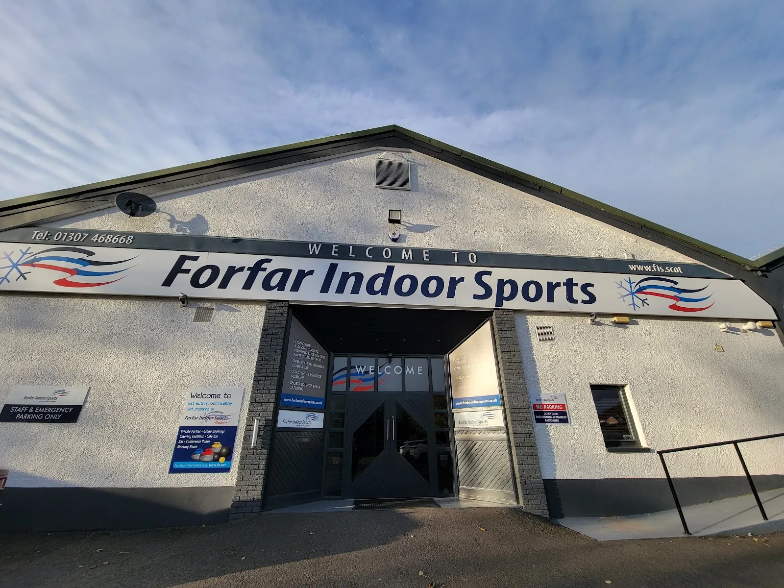 The white-harled front of Forfar Indoor Sports with the long 'Welcome to Forfar Indoor Sports' sign above the dark entrance doorway, seen from the car park. — Forfar Indoor Sports (Ice World)