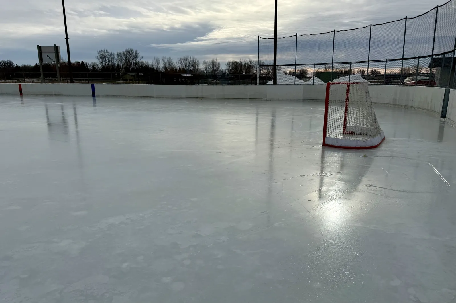 La pista de hielo exterior de Fosston con una portería de hockey sobre el hielo y focos que se reflejan en la superficie. — Fosston Outdoor Ice Rink