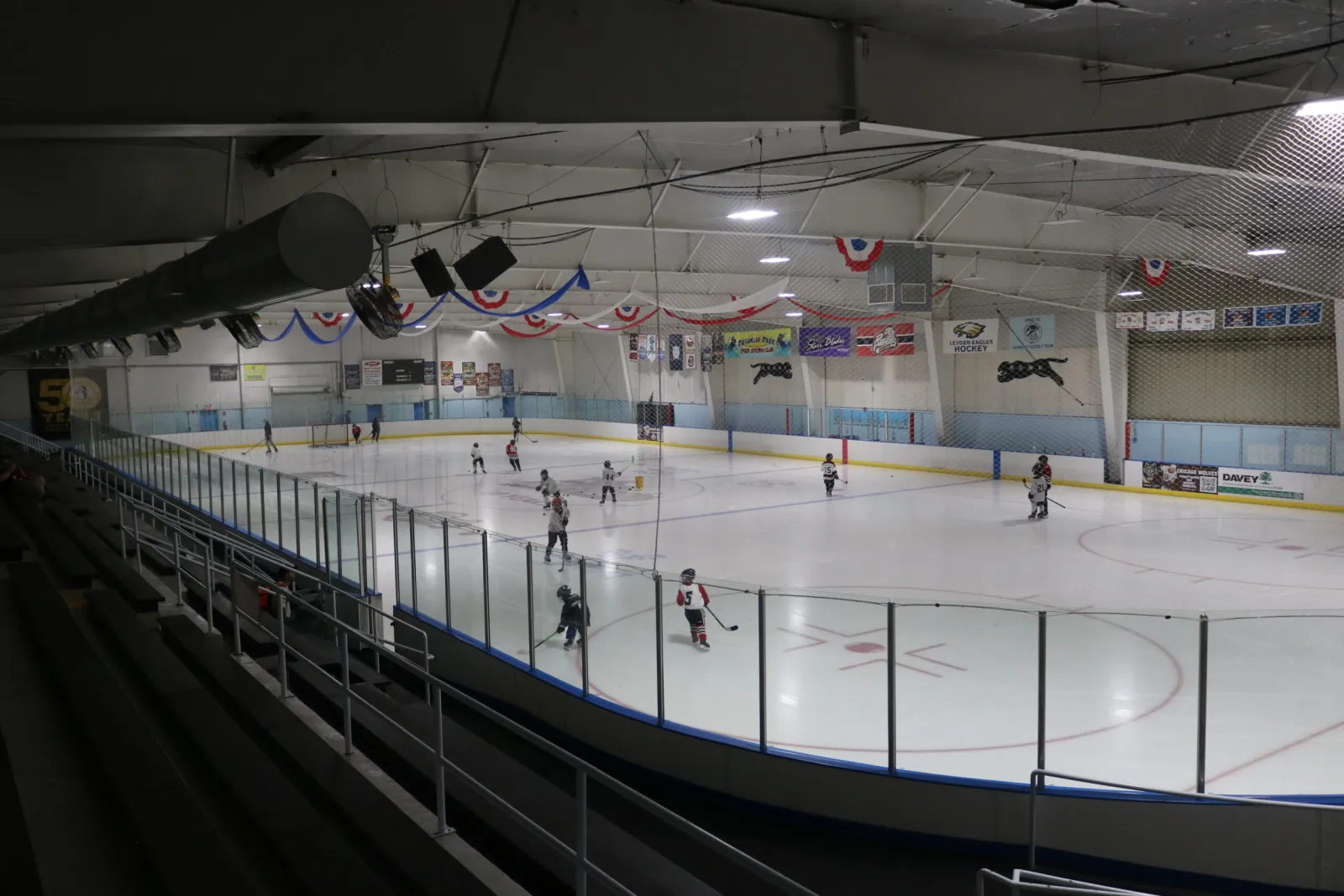 Youth hockey players on the full ice sheet, with team banners including Leyden Eagles Hockey and a 50-years anniversary banner visible on the end wall — Franklin Park Ice Arena