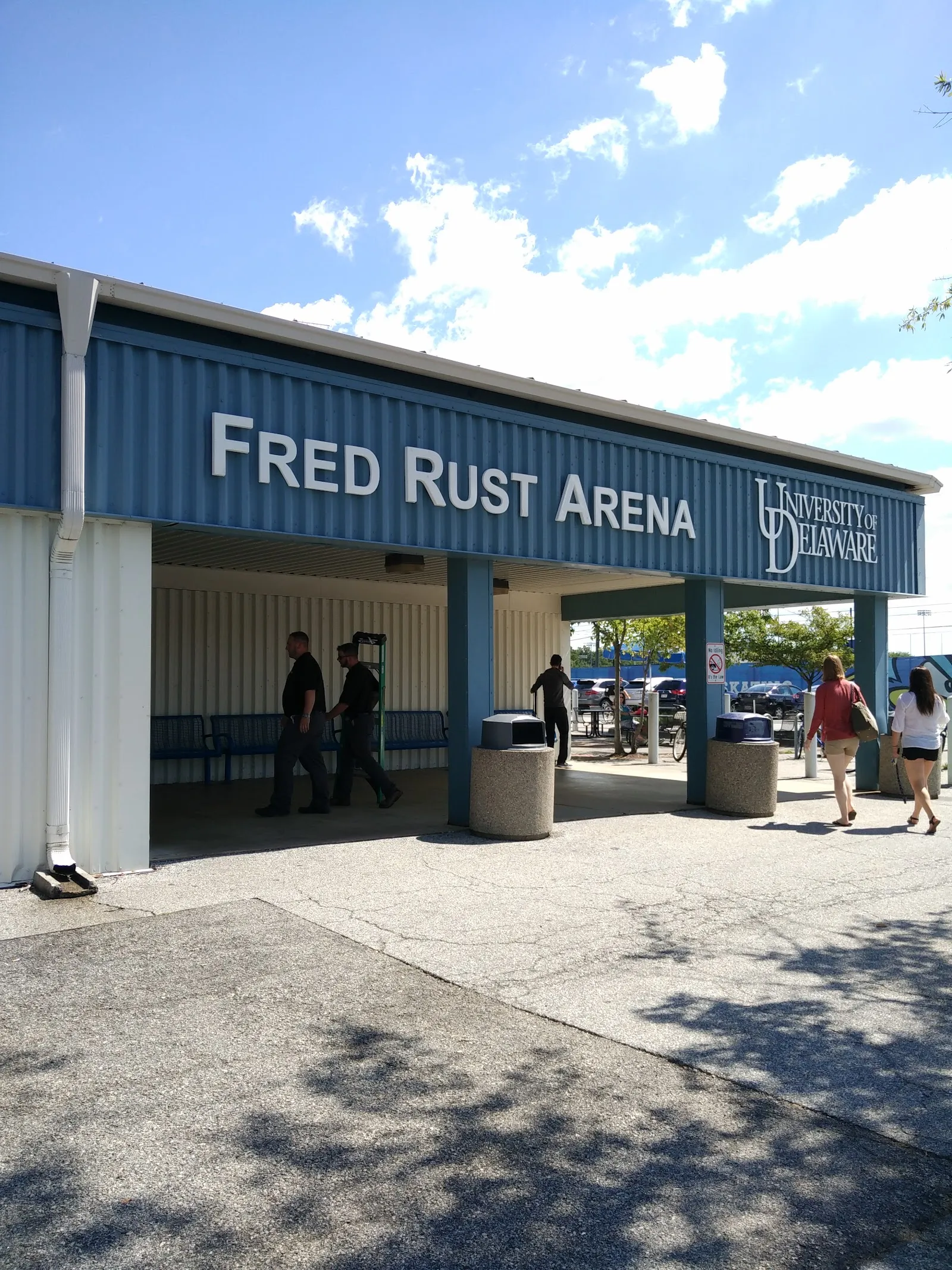 The covered blue entrance of Fred Rust Arena with the University of Delaware name on the fascia, seen from the forecourt — Fred Rust Ice Arena