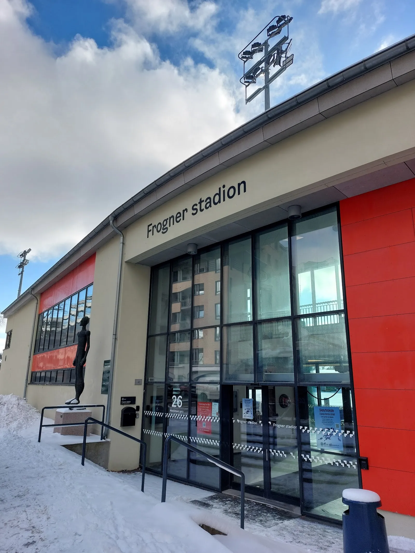 Den glassede inngangen til Frogner stadion i Oslo med navnet i bokstaver på den kremfargede veggen ved siden av et rødt panel, sett fra den snødekte stien — Frogner stadion