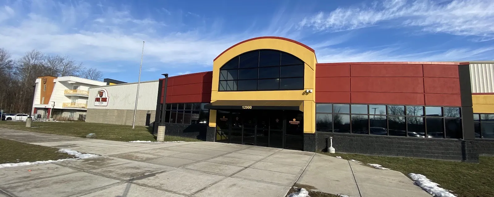 The Fuel Tank entrance at 12900 Fuel Way, a yellow arched front with tall windows set in a long red building, the rink's sign on the wing behind — Fuel Tank at Fishers