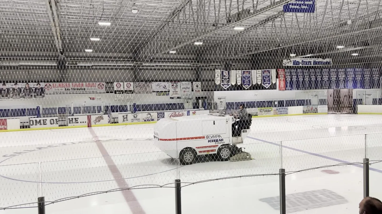 The ice at Galactic Ice with the resurfacer at work, seen through the safety netting with the banners and boards along the far side — Galactic Ice