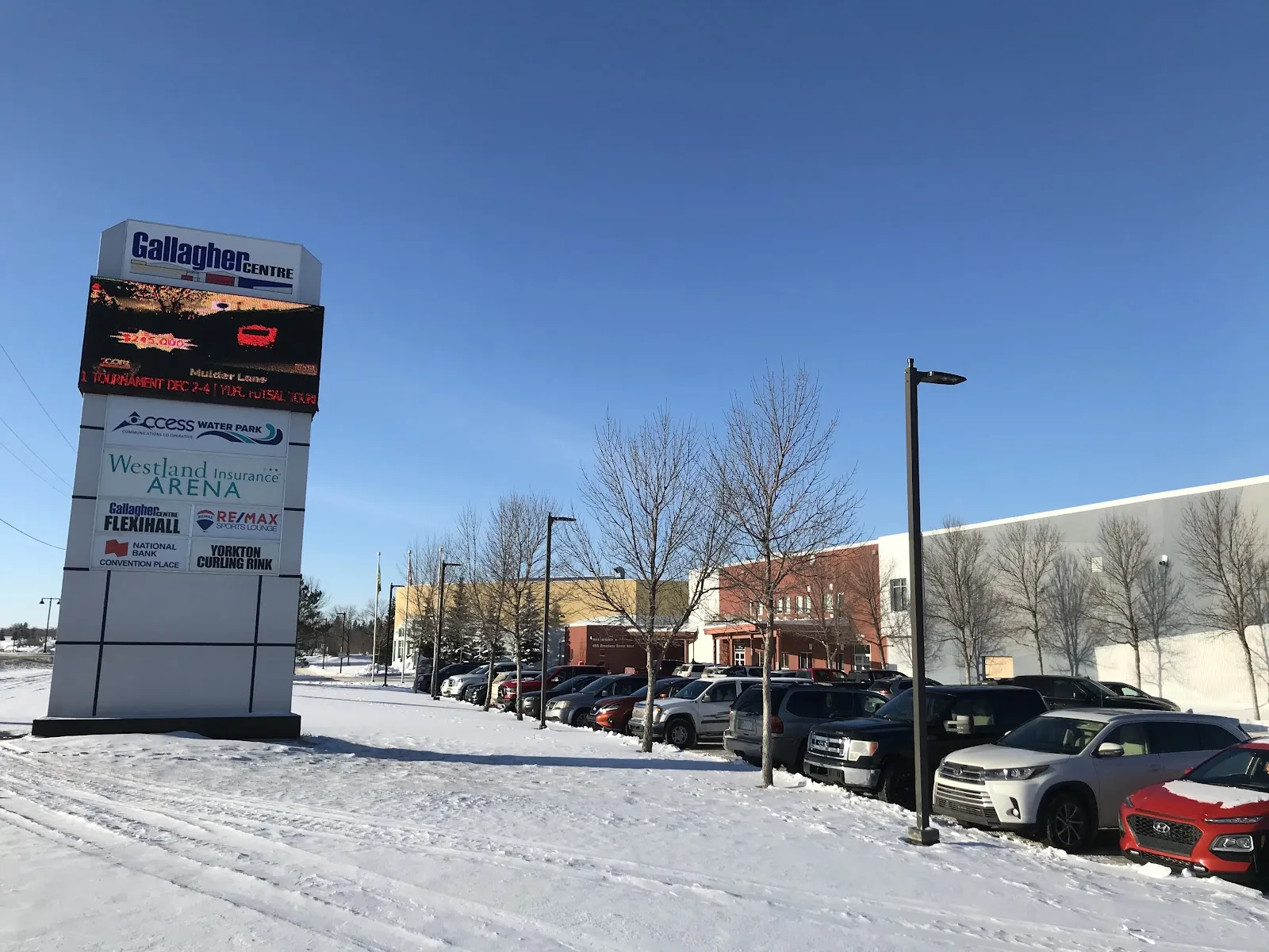 The Gallagher Centre pylon sign listing the Access Water Park, Westland Insurance Arena, Flexihall and curling rink, with the building and a snowy parking lot behind. — Gallagher Centre