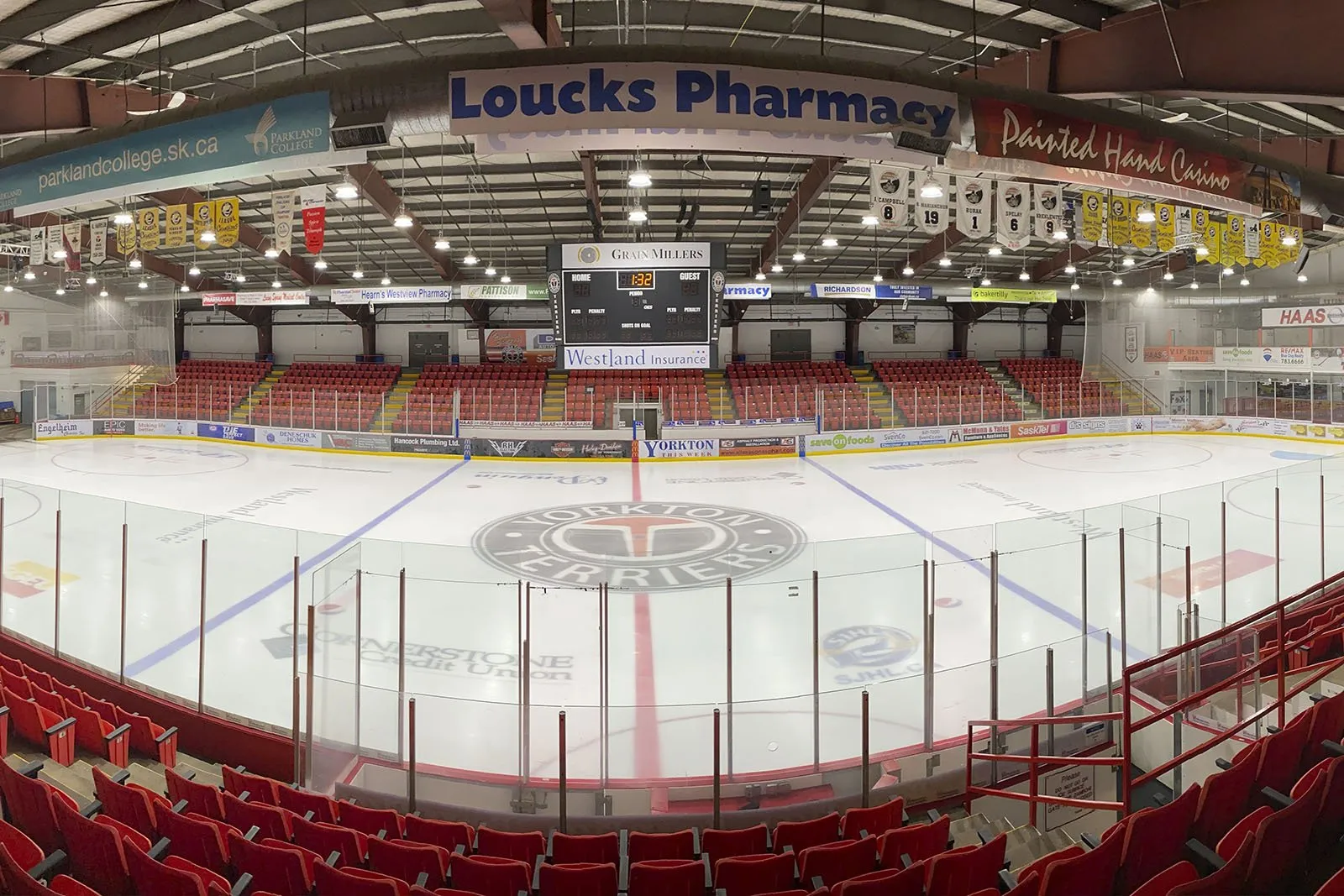 The Gallagher Centre arena from the stands: the Yorkton Terriers logo at centre ice, red seats around the rink and sponsor banners below the scoreboard. — Gallagher Centre