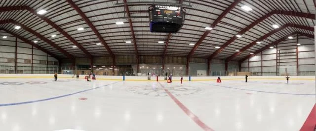 Panoramic view of the Gallatin ice sheet under red roof trusses and a hanging scoreboard, before the current expansion. — Gallatin Ice