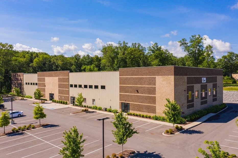 Brick-and-metal arena building beside the parking lot and tree line — Gary Force Acura Ice Arena