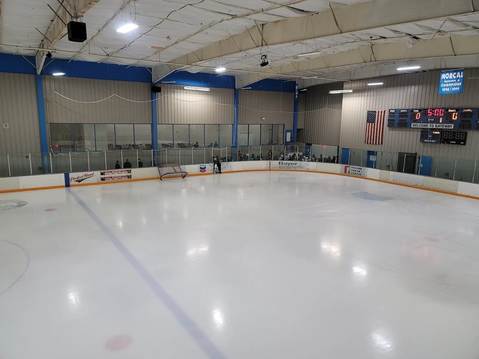 La pista de hielo vista desde las vallas, con el marcador y la bandera de Estados Unidos en la pared del fondo. — Gateway Ice Center