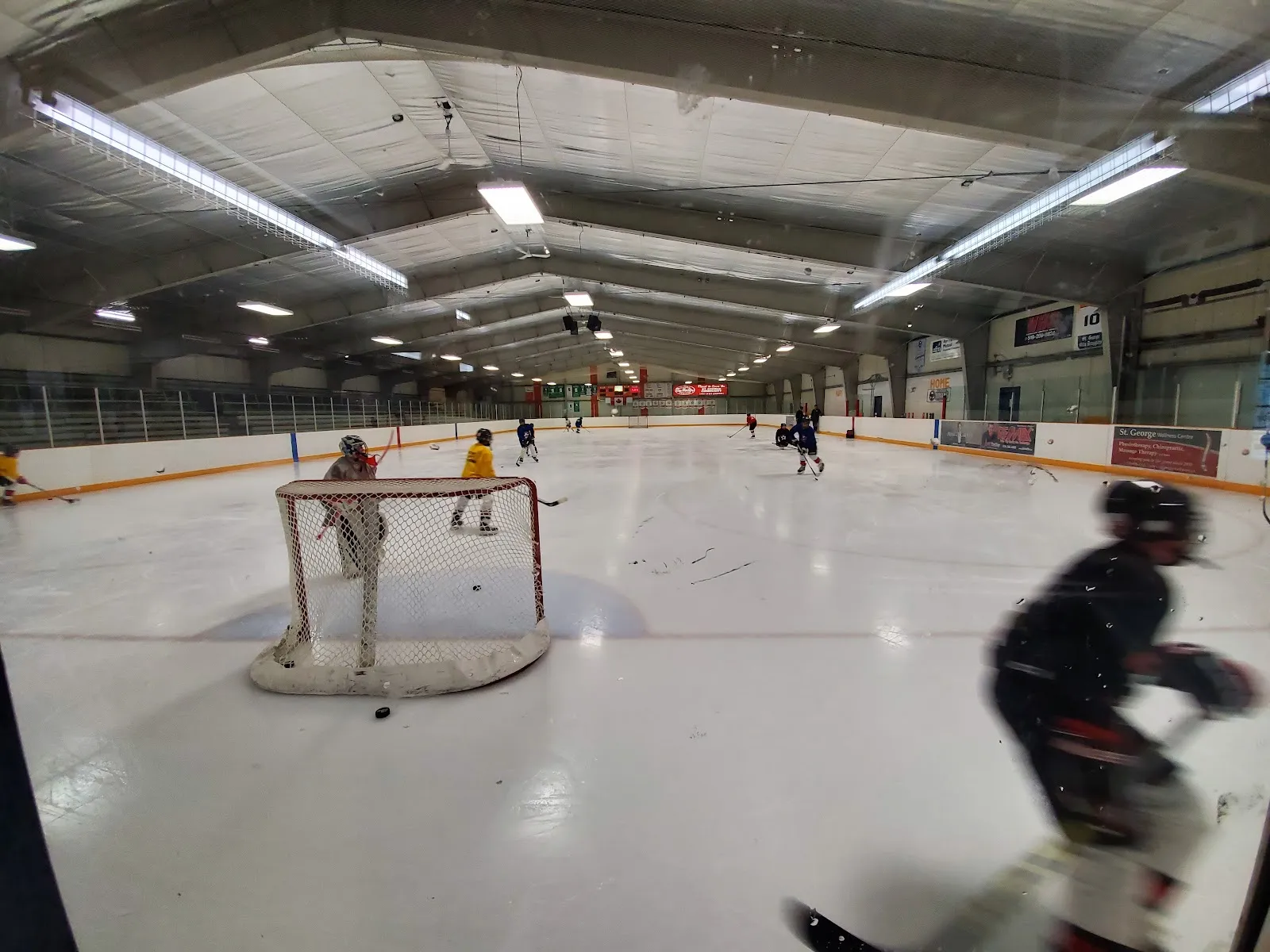 The arena ice at Gaukel Memorial Community Centre seen from behind the glass, with a net in the foreground and skaters farther down the sheet. — Gaukel Memorial Community Centre