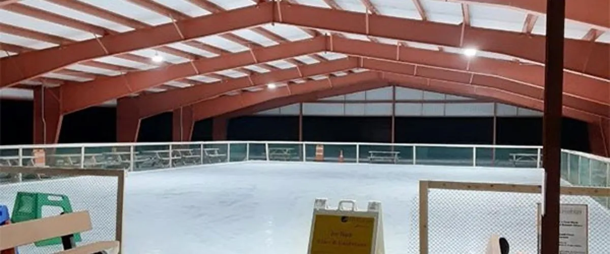 The covered rink at Gavin Park in Wilton under its red steel roof, with the boards, benches and an empty ice surface. — Gavin Park Ice Rink