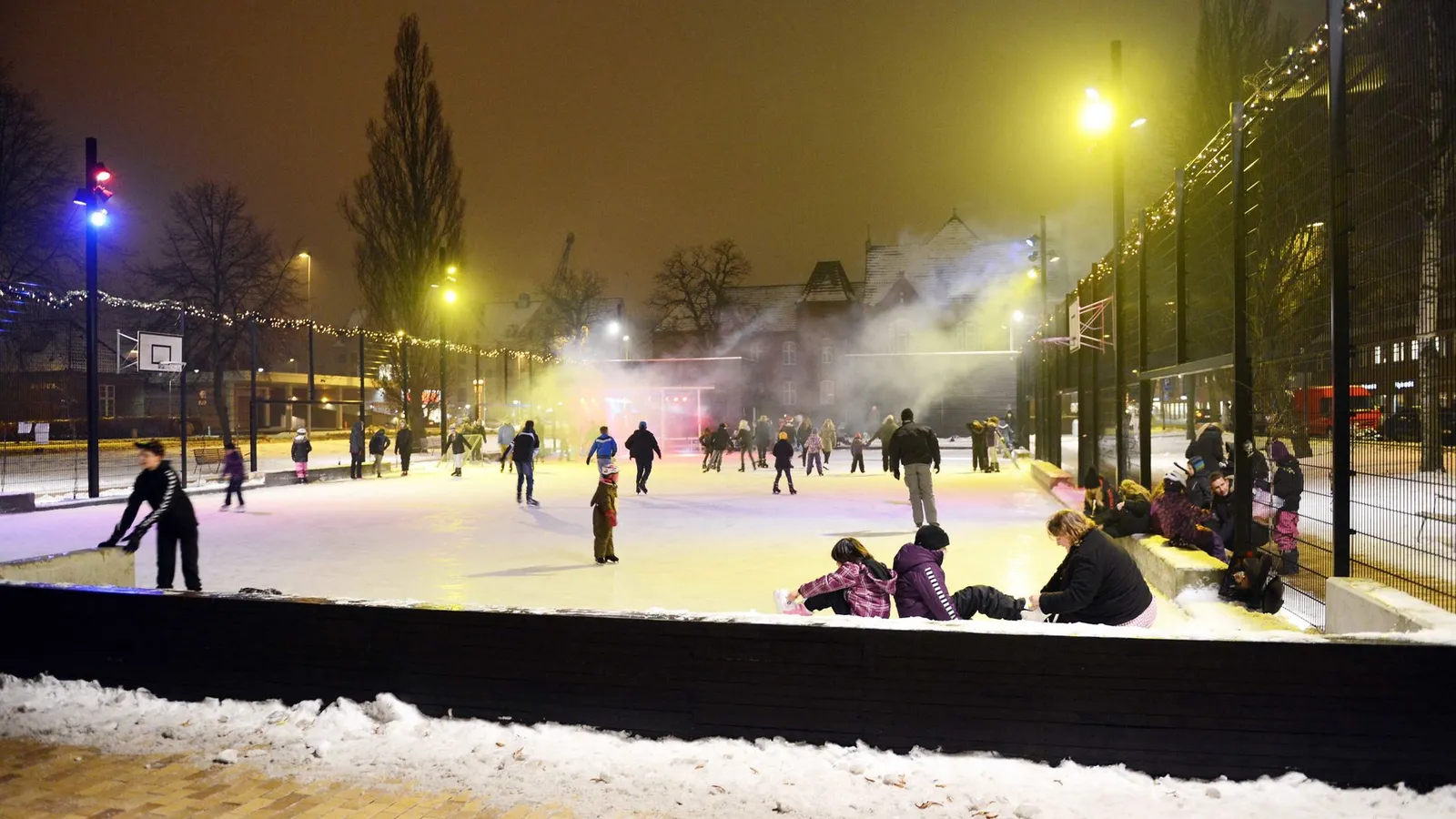 The Genforeningshaven ice rink in Aabenraa at night, with skaters in the distance on the lit ice and misty floodlights beyond. — Genforeningshaven Skøjtebane