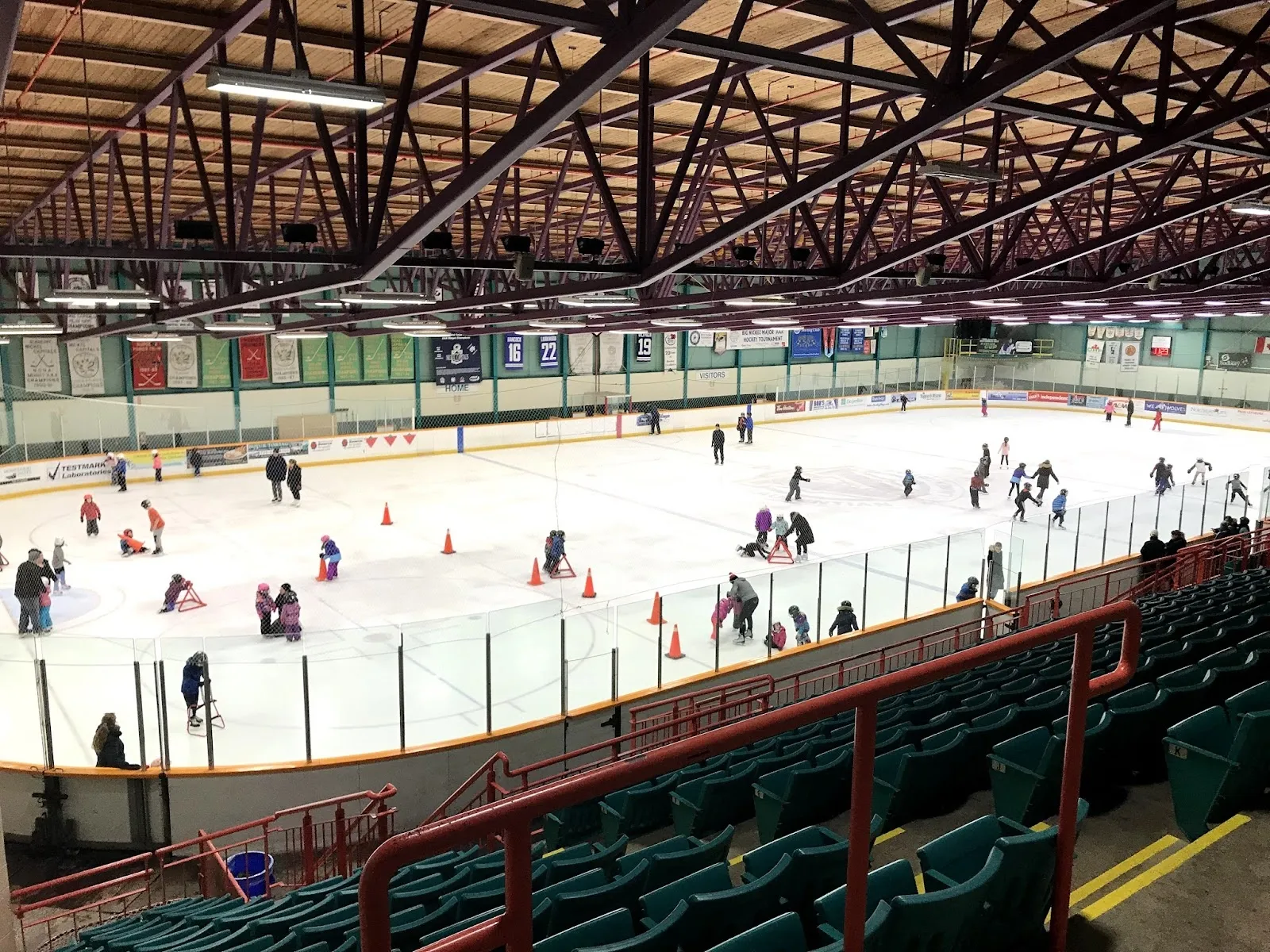 A public session in the arena seen from the green seats, skaters spread across the sheet among cones under a dark timber-trussed roof. — Gerry McCrory Countryside Sports Complex