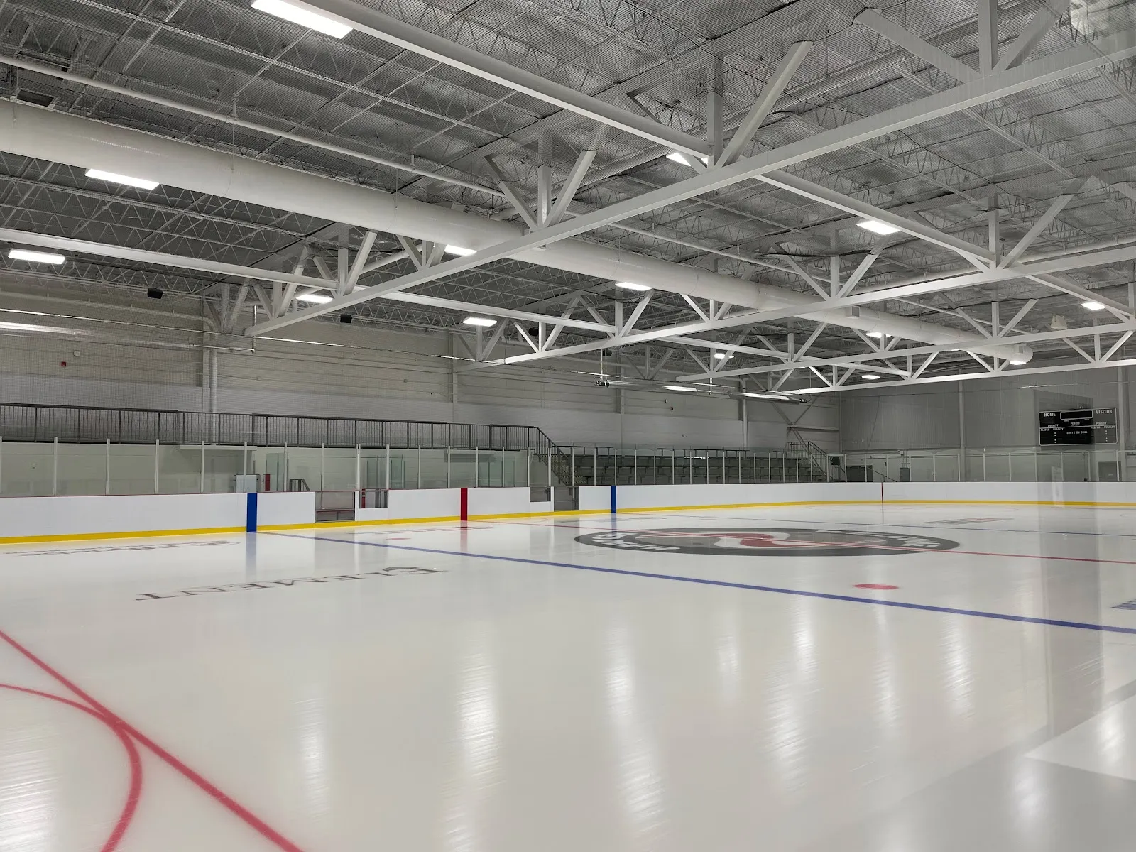 Una arena vacía con líneas recién pintadas bajo armaduras blancas de acero, con un logotipo en el centro de la pista y vallas transparentes alrededor de la pista. — G.H. Dawe Community Centre