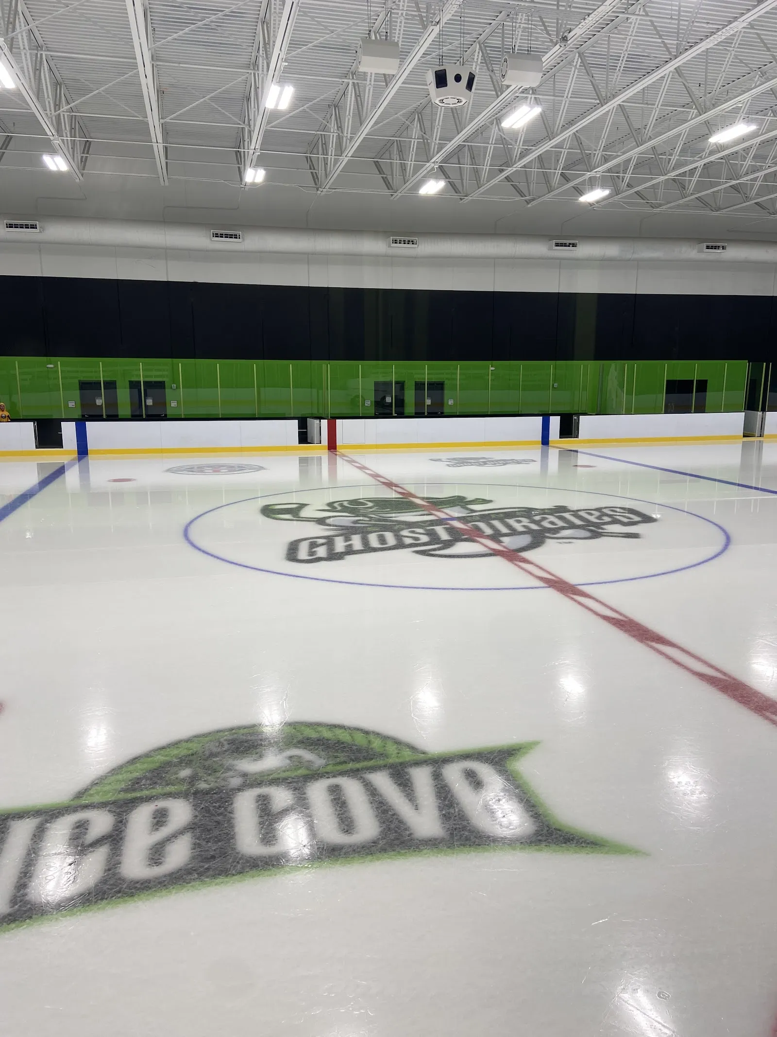 The empty ice at Ghost Pirates Ice Cove with the team logo at centre ice and the green and black wall behind the boards — Ghost Pirates Ice Cove