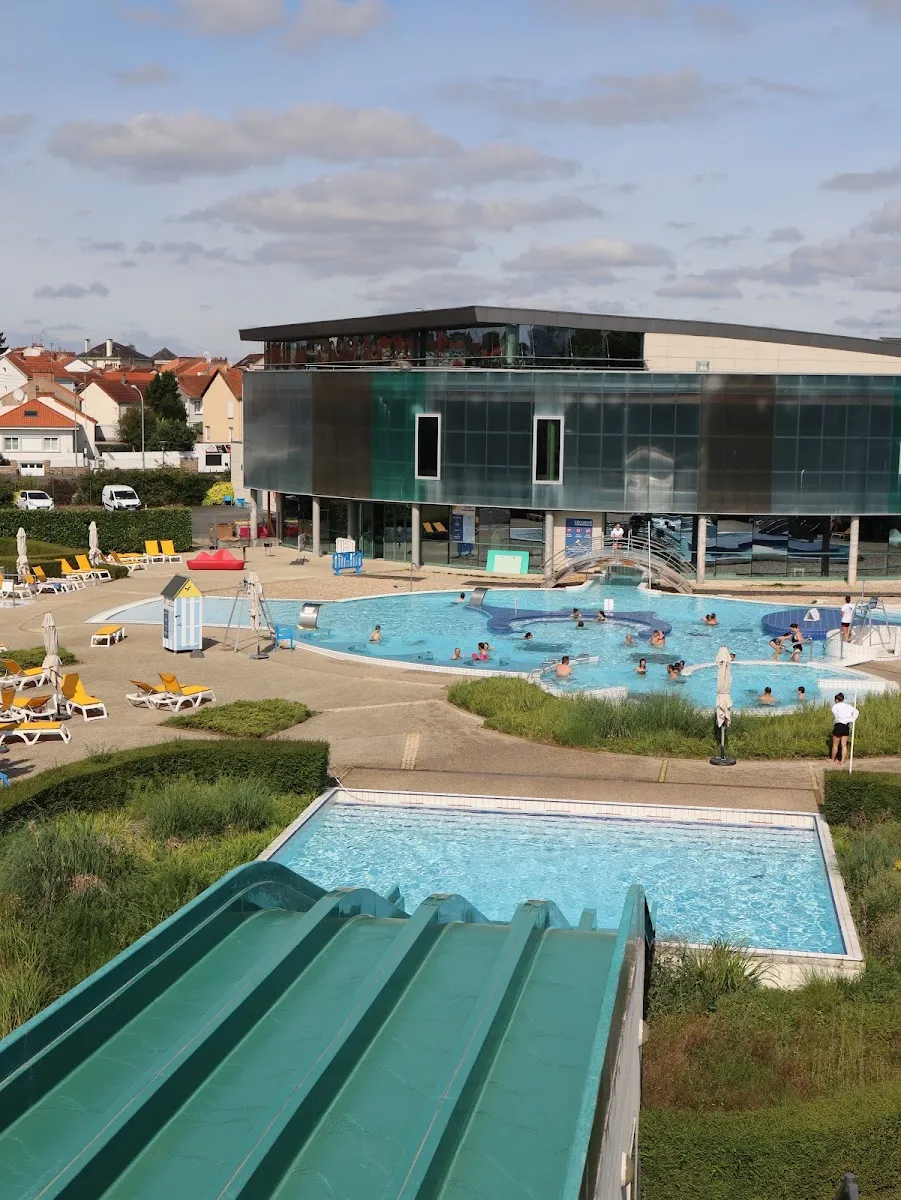 Le complexe de loisirs Glisséo vu de dessus son bassin extérieur, avec le toboggan aquatique vert au premier plan et le bâtiment en verre et en acier derrière. — Glisséo Patinoires