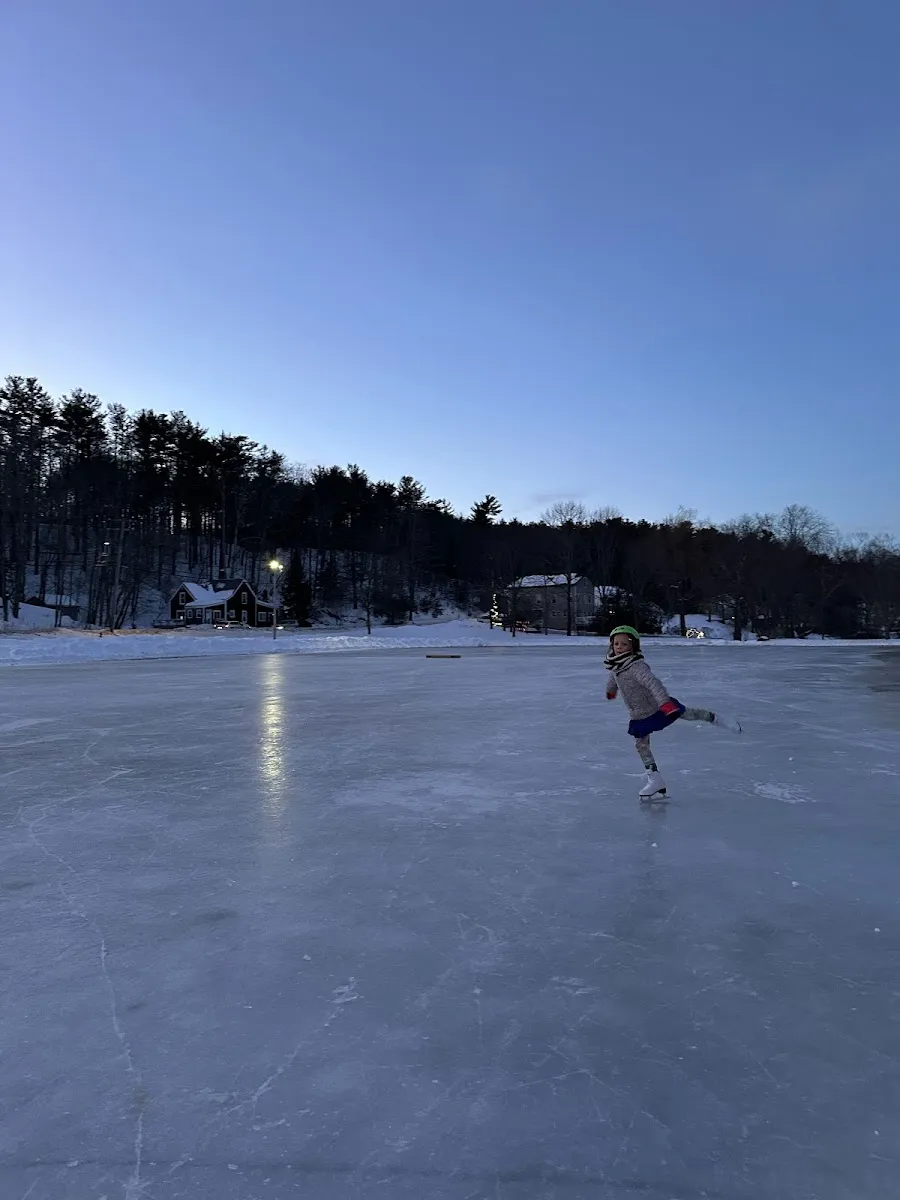 Skater on the plowed ice of Goddard's Pond in Bath, Maine, with the wooded shoreline behind — Goddards Pond Ice Rink