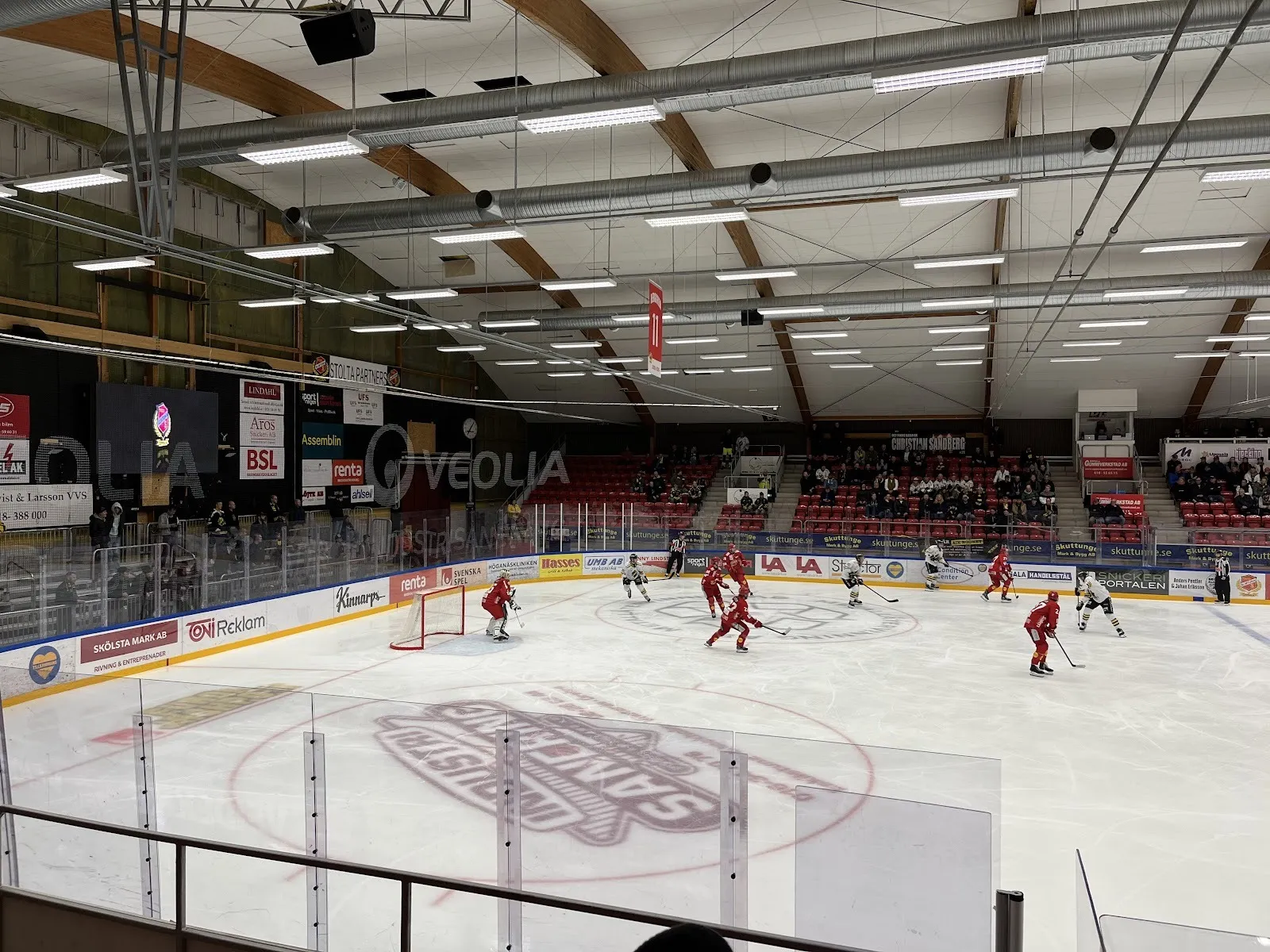 En match pågår i Gränby ishall, spelare i rött och vitt kring målet under taket av trä och stål med åskådare bakom sargen. – Gränby ishallar