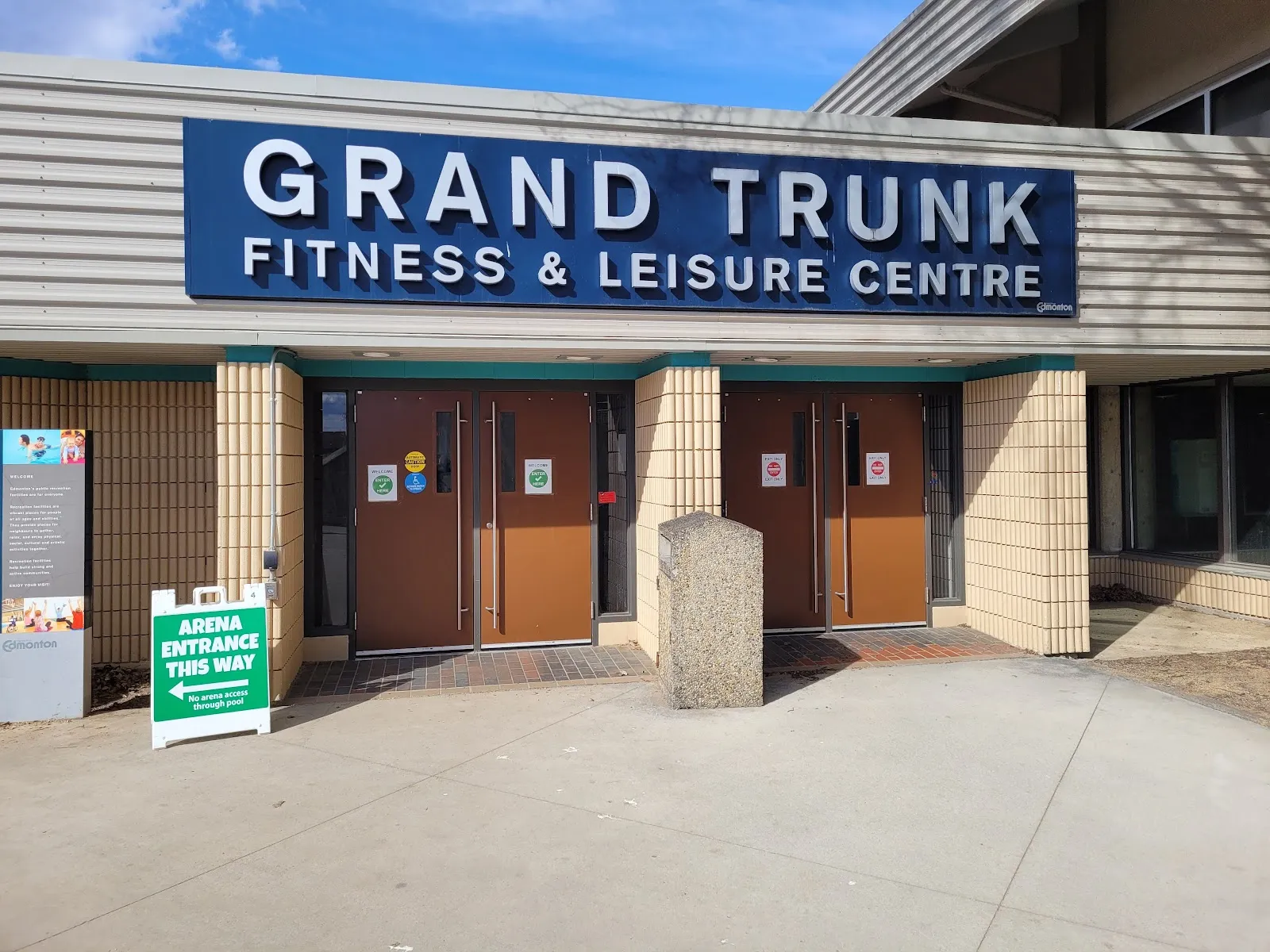 Entrance of the Grand Trunk Fitness & Leisure Centre building, with a large wall sign reading "Grand Trunk Fitness & Leisure Centre" and a sandwich-board sign reading "Arena Entrance This Way" pointing to the doors. — Grand Trunk Arena